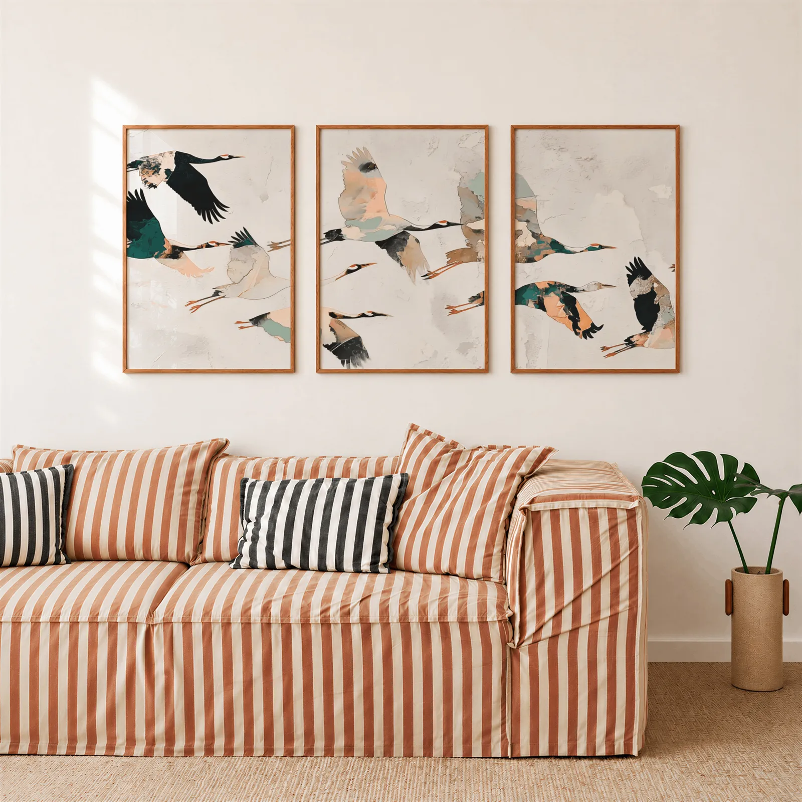 crane birds triptych wall art, above a rust-striped sofa beside a potted monstera
