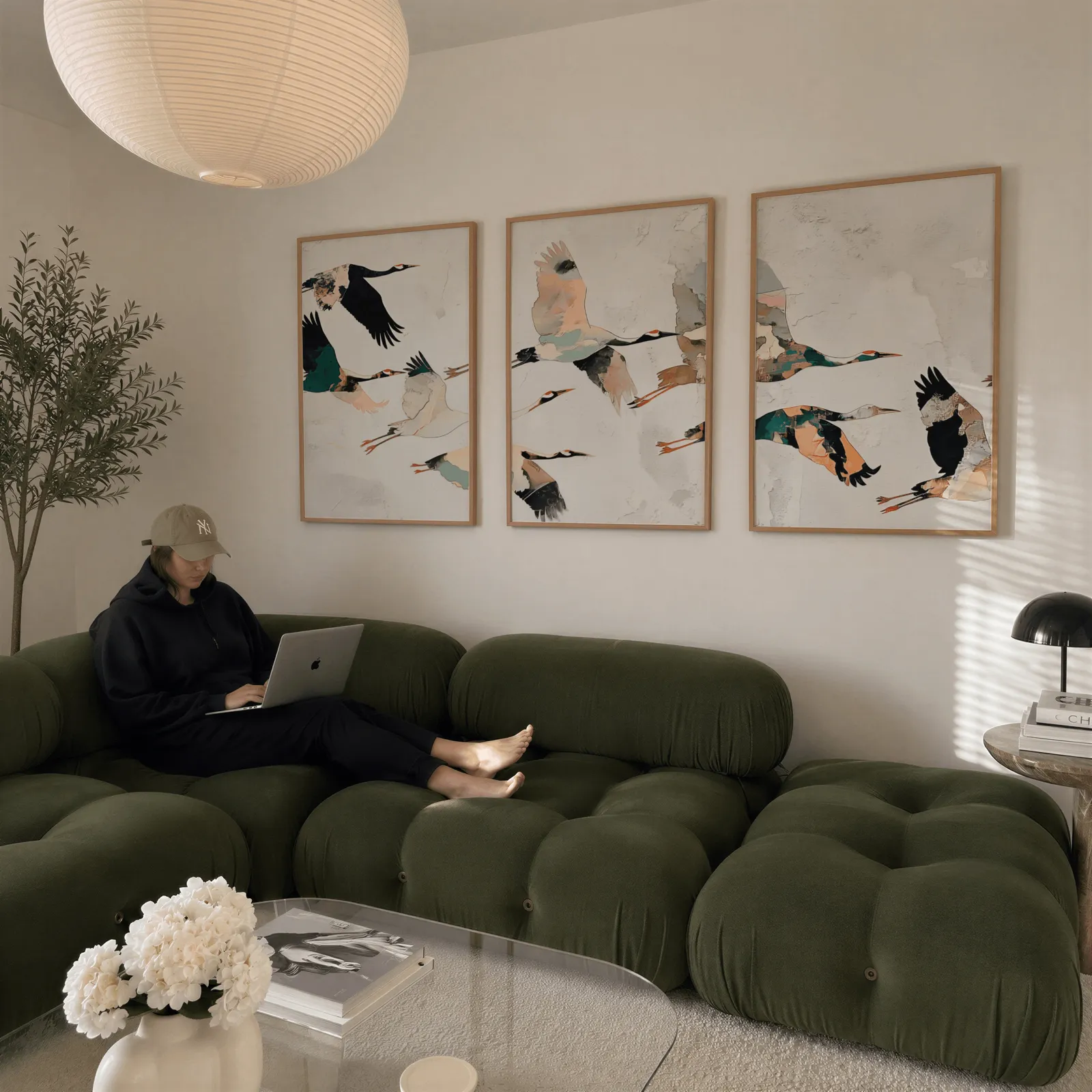 crane birds triptych wall art, above a plush olive velvet sectional beneath a paper lantern light