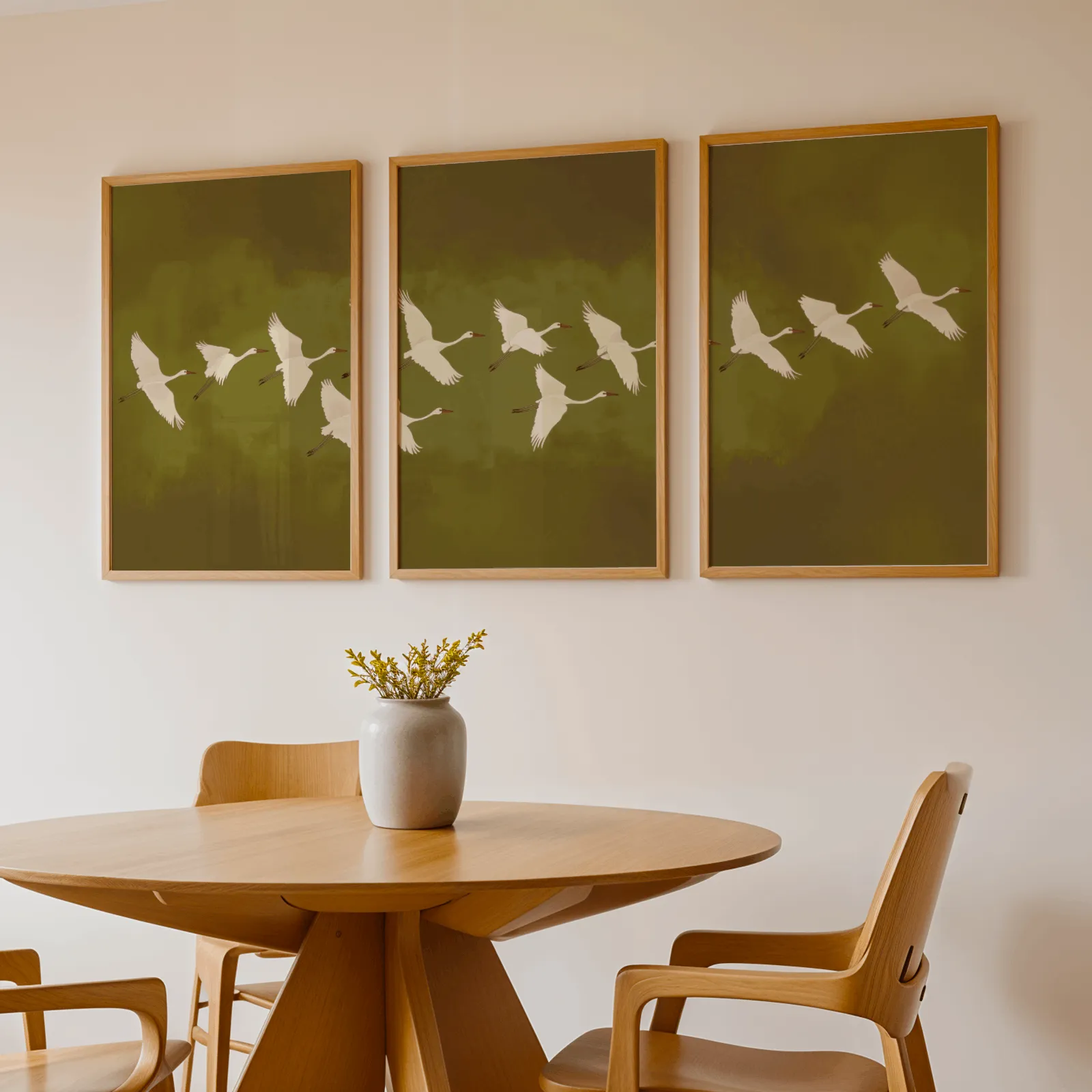 green cranes triptych wall art, above a round wooden table with a stoneware vase