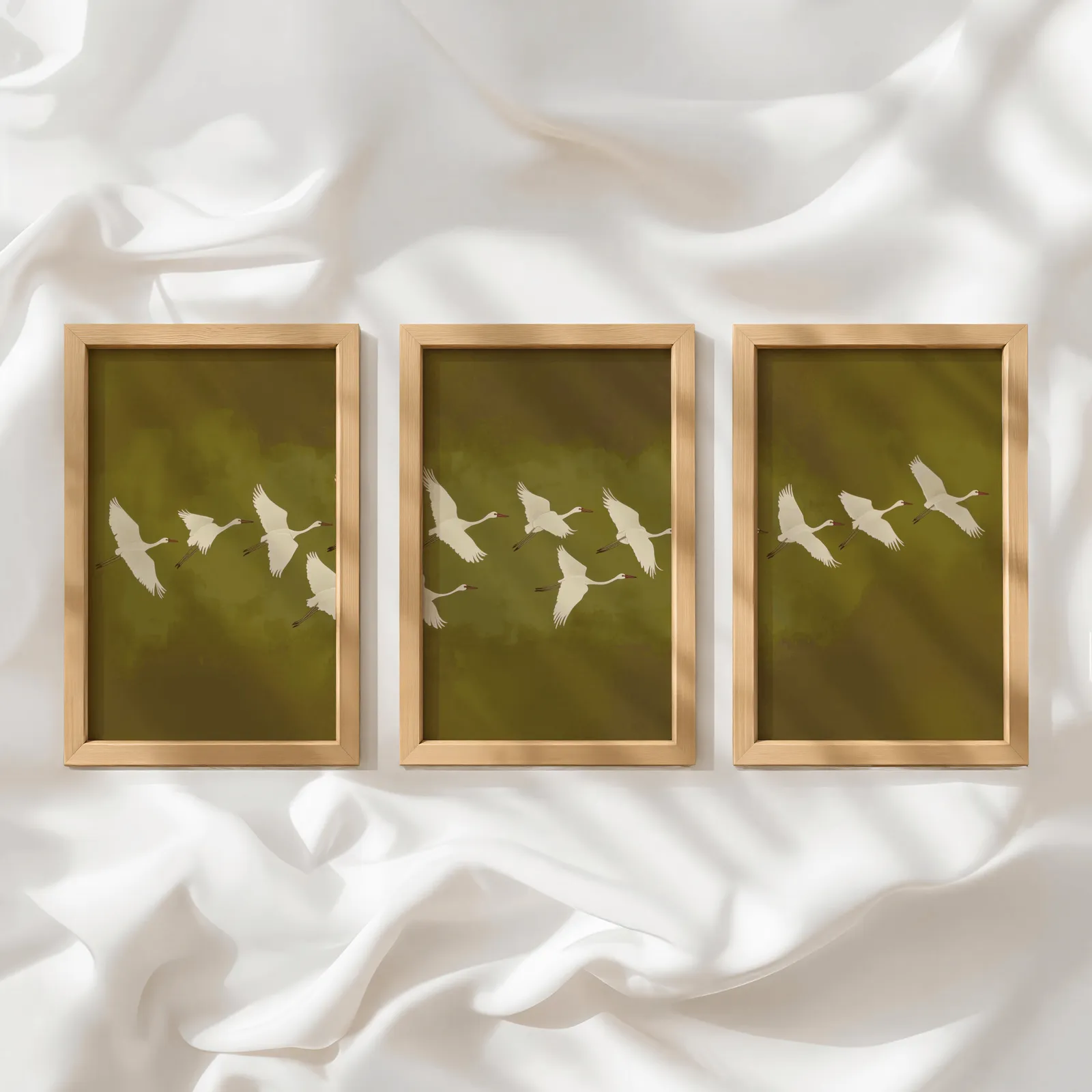 green cranes triptych wall art, in a row atop rumpled white silky fabric