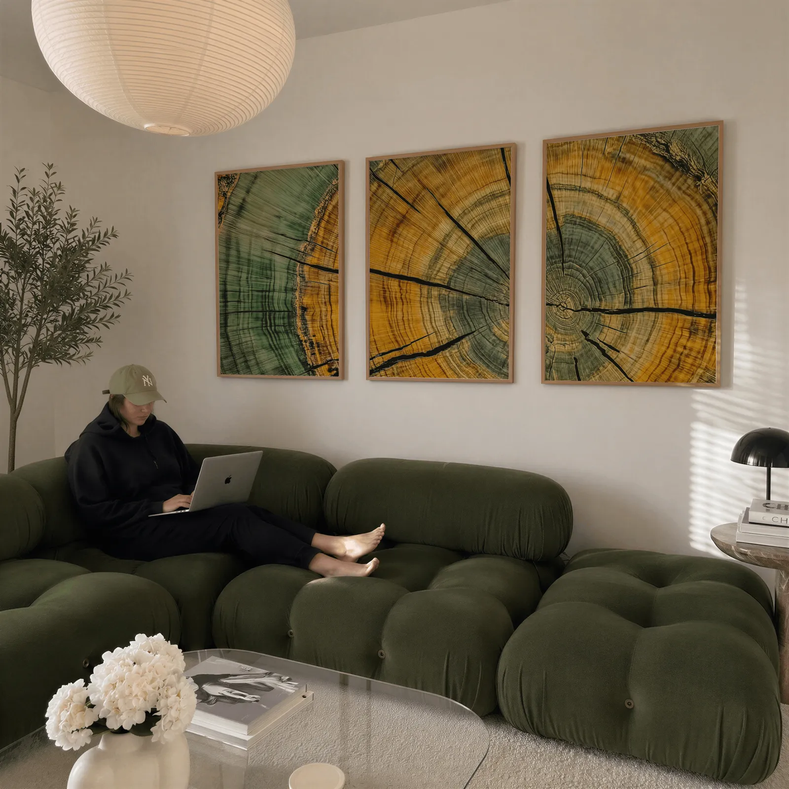 green and yellow tree rings wall art set of 3, above a plush olive velvet sectional beneath a paper lantern light
