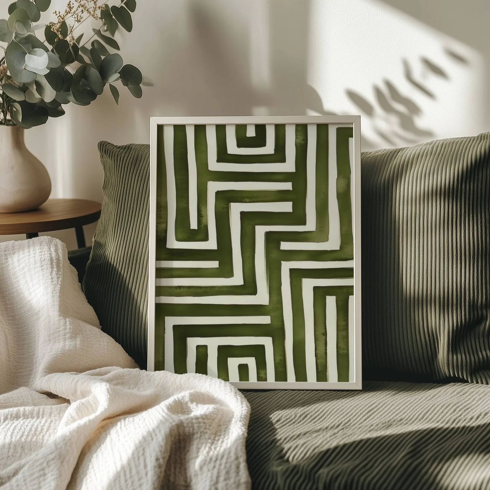 green abstract maze minimalist wall art, propped on an olive corduroy sofa beside a eucalyptus vase