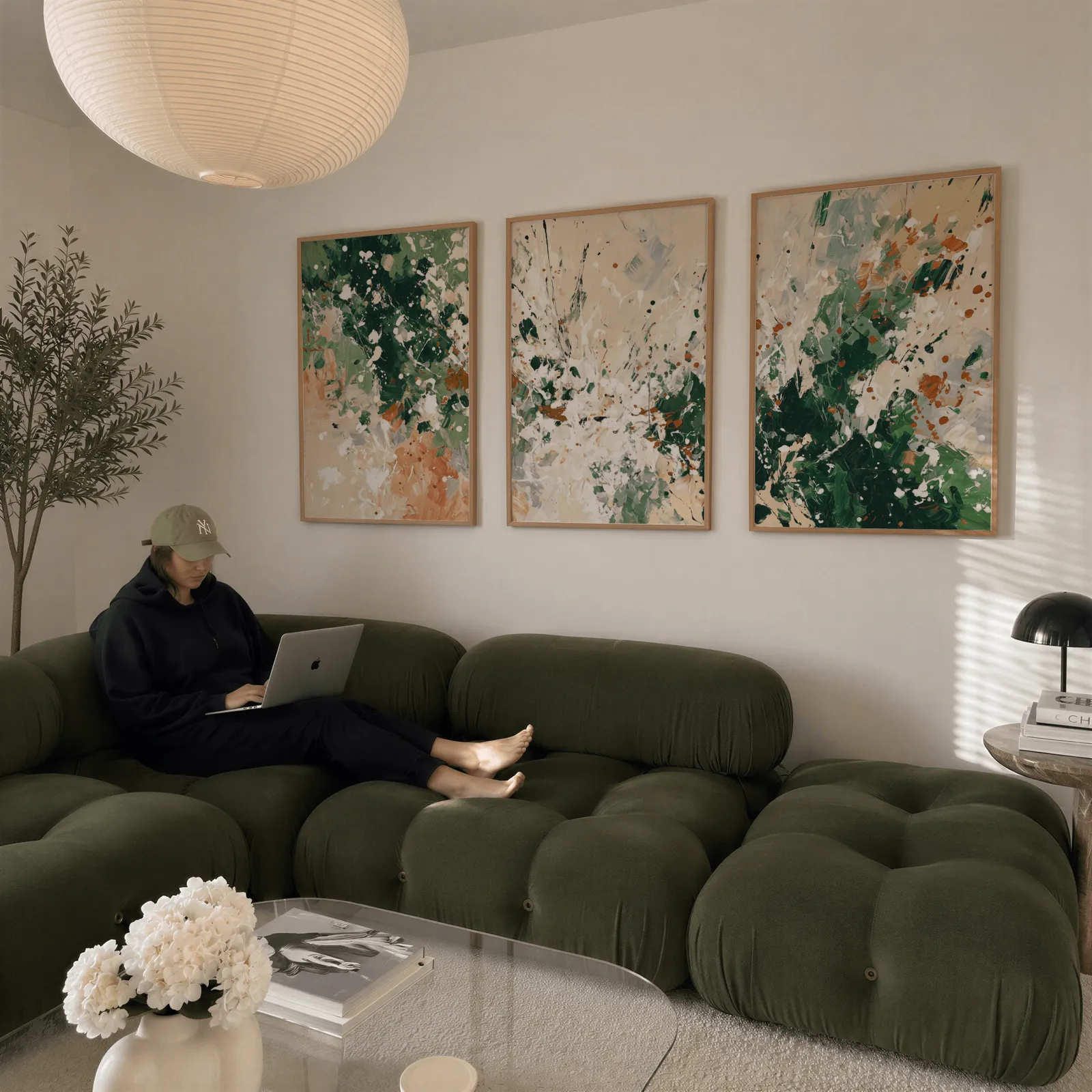 green terracotta abstract wall art set of three, above a plush olive velvet sectional beneath a paper lantern light