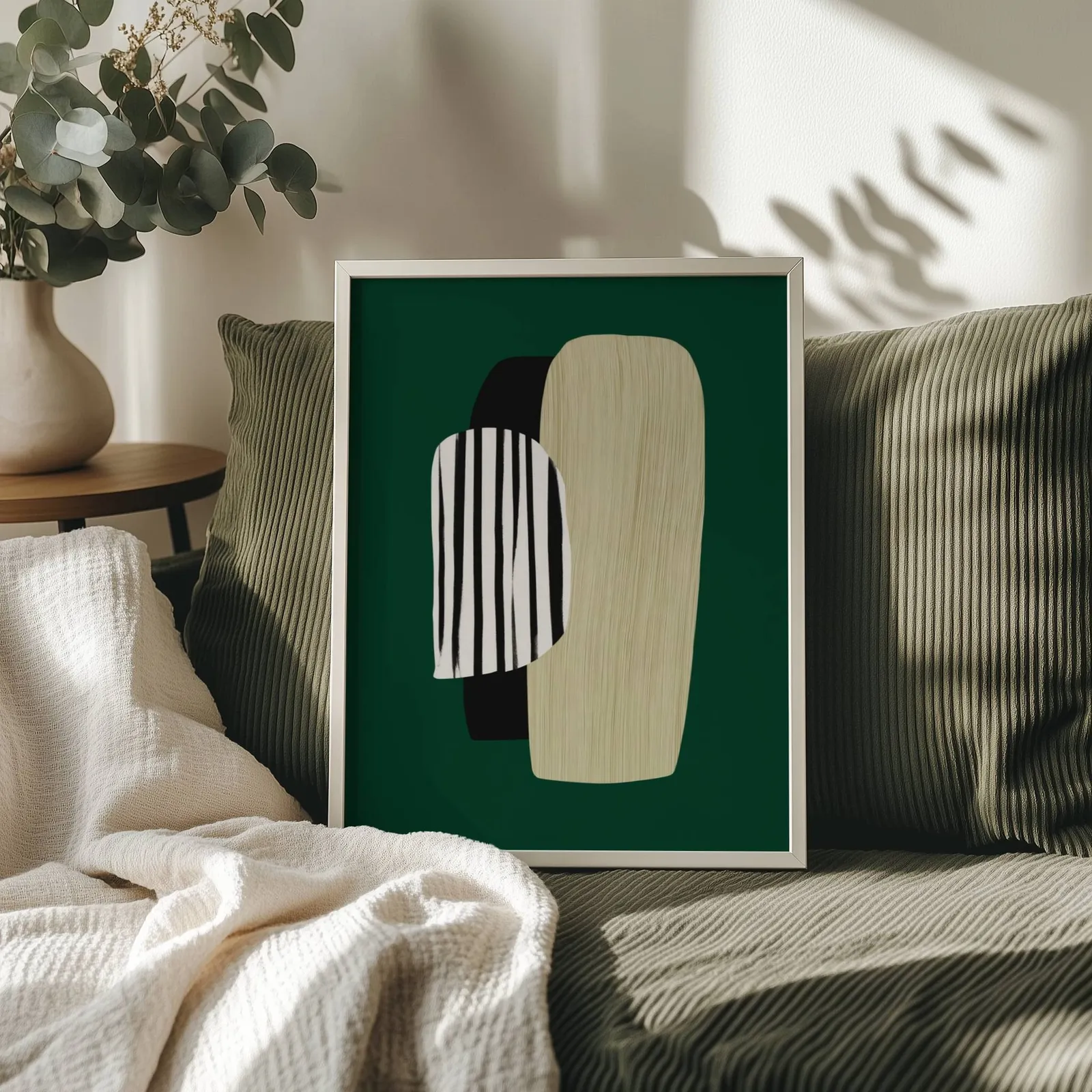 green abstract minimalist wall art with totem shapes, propped on an olive corduroy sofa beside a eucalyptus vase