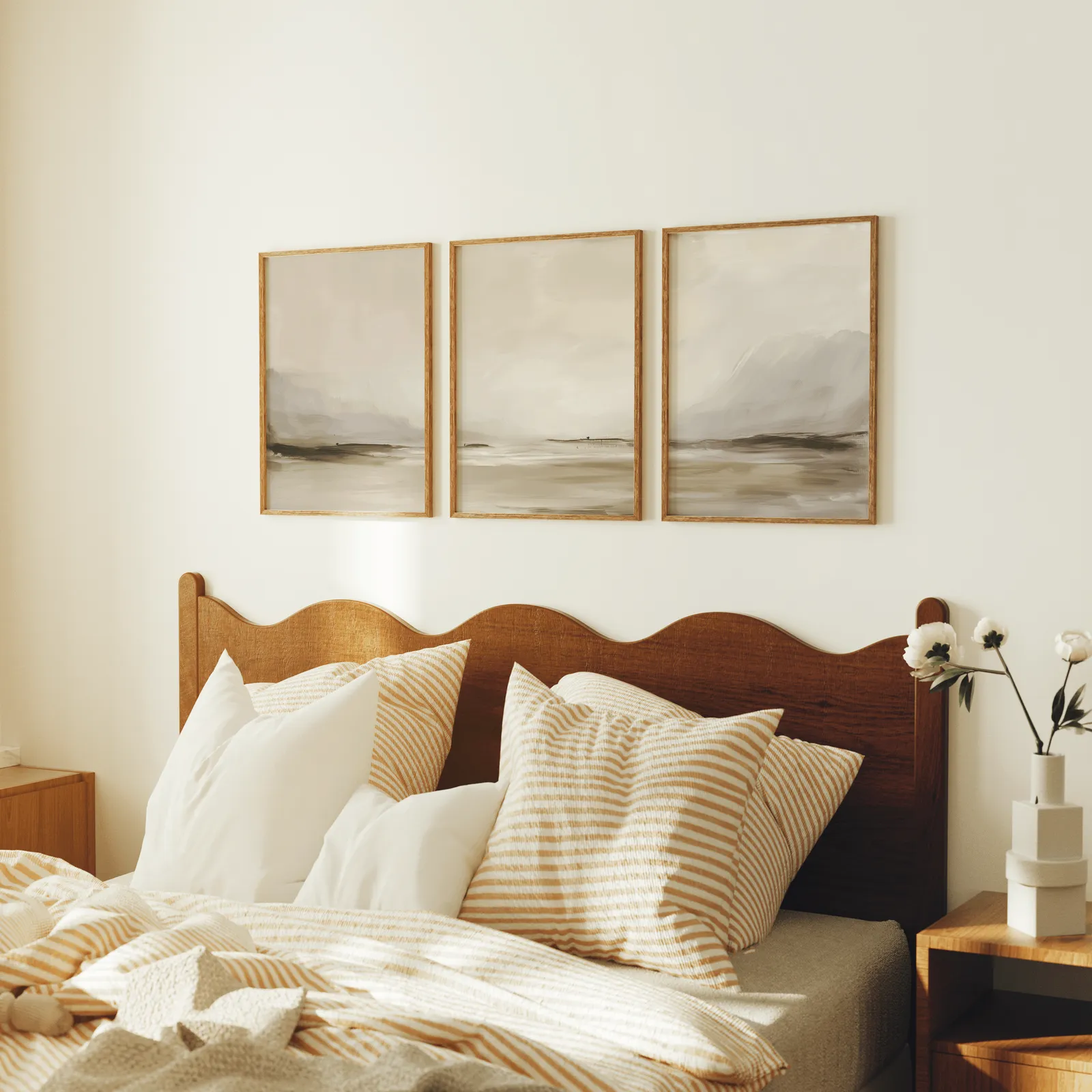 neutral coastal landscape triptych wall art, above a scalloped wooden headboard with striped pillows