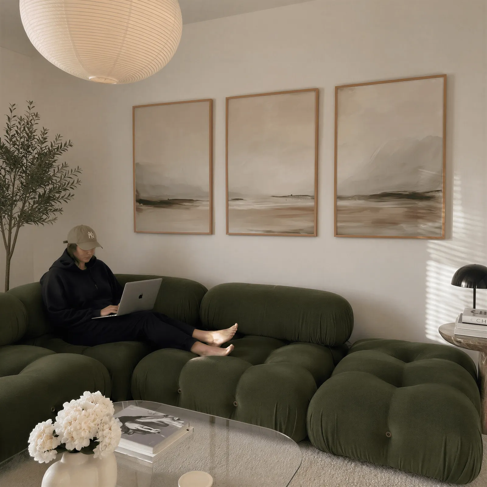 neutral coastal landscape triptych wall art, above a plush olive velvet sectional beneath a paper lantern light