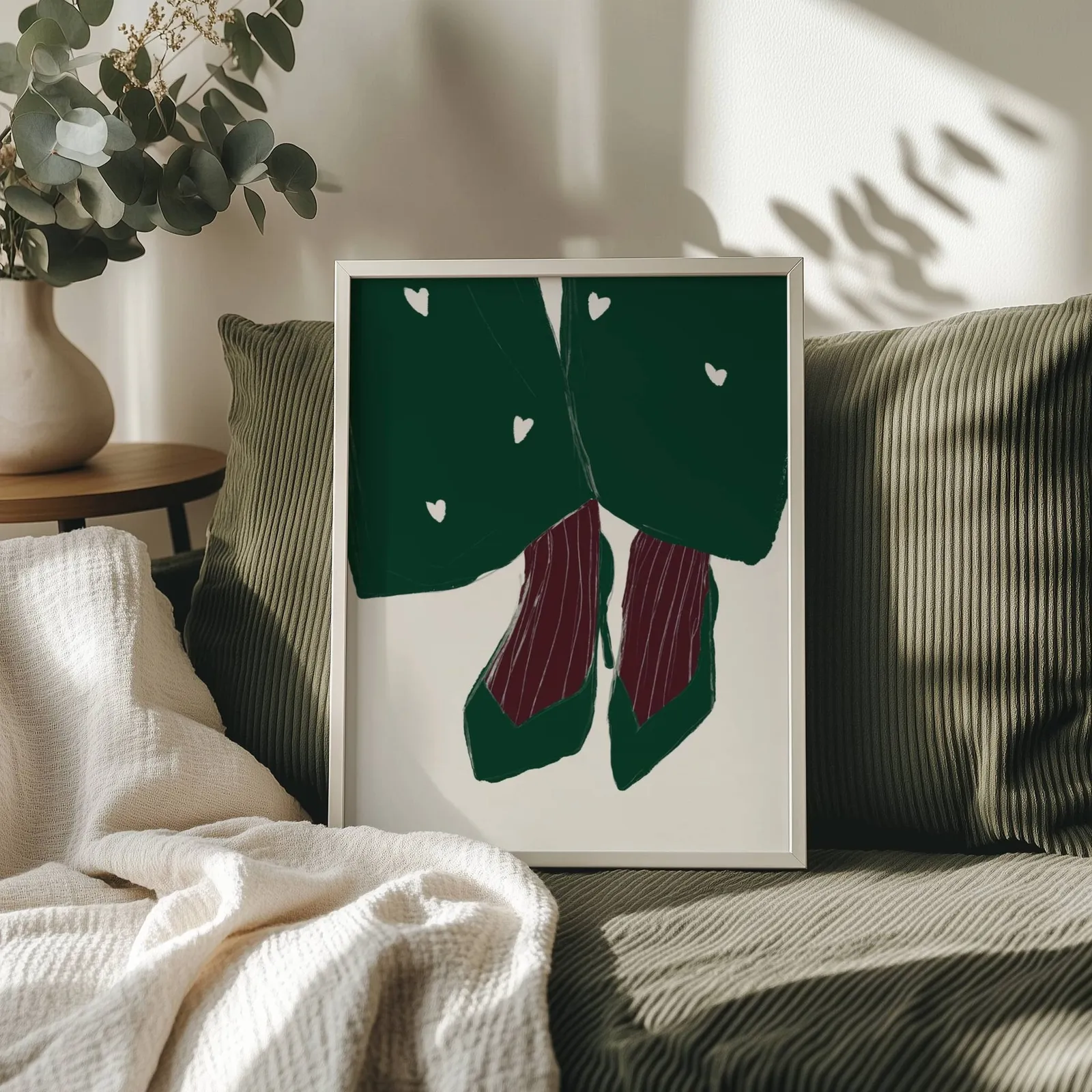 green heart pattern coat with burgundy heels wall art, propped on an olive corduroy sofa beside a eucalyptus vase