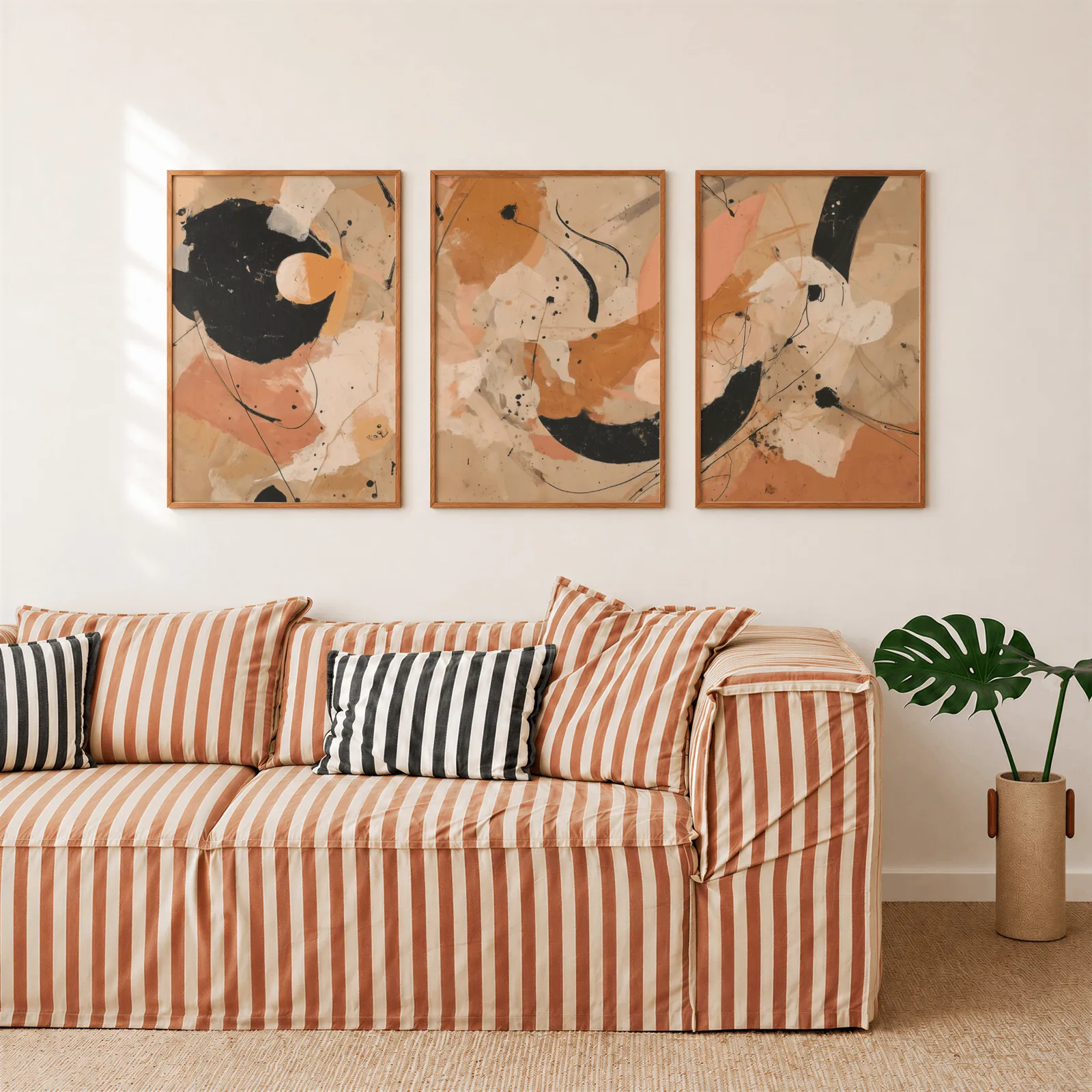 terracotta black abstract three piece wall art, above a rust-striped sofa beside a potted monstera