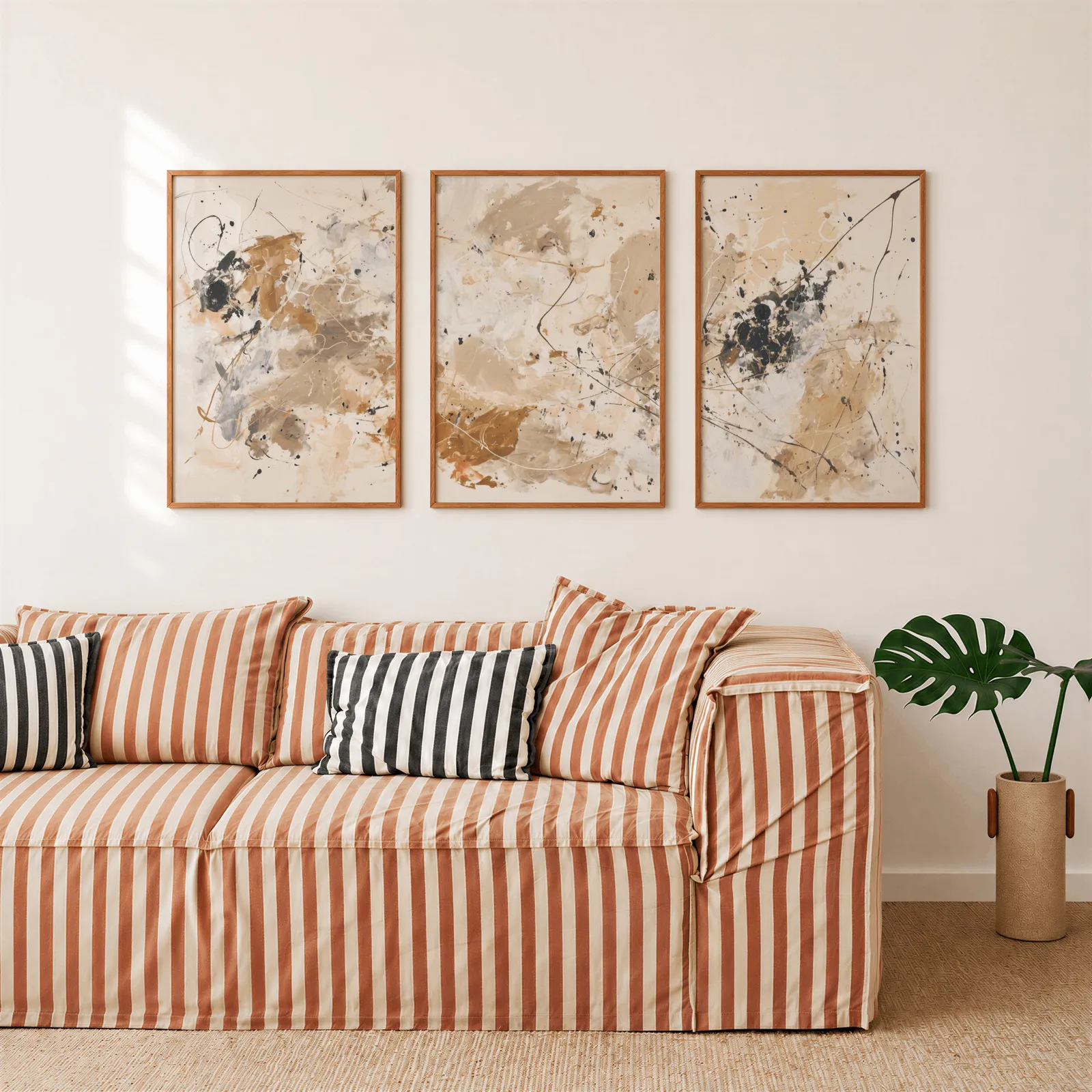 beige and black abstract triptych wall art, above a rust-striped sofa beside a potted monstera