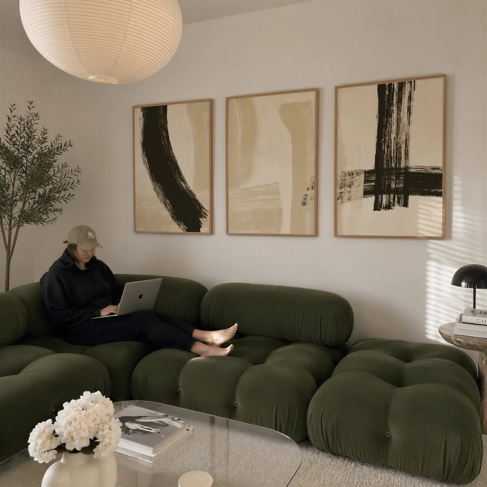 black and beige abstract minimalist triptych wall art, above a plush olive velvet sectional beneath a paper lantern light