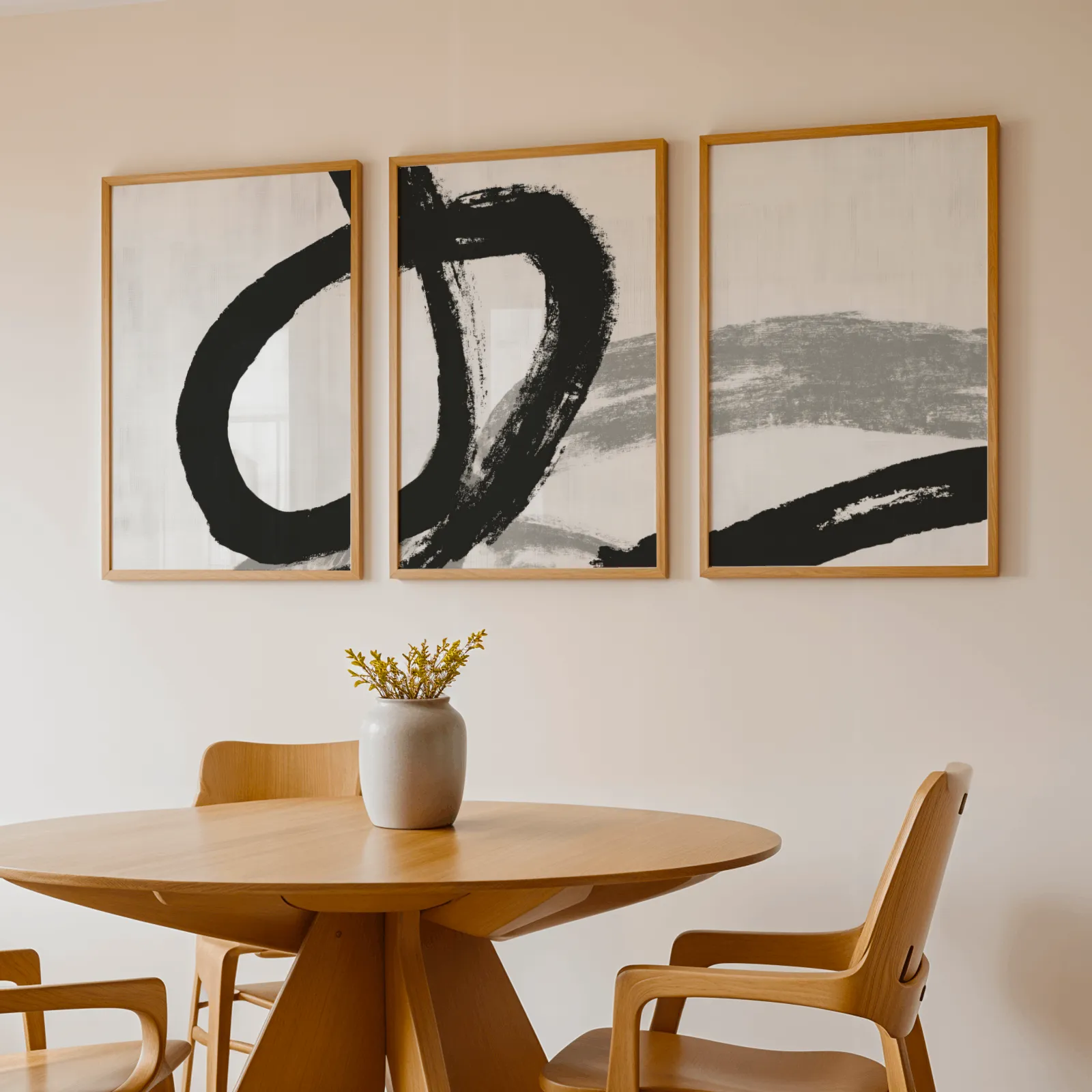 black and white minimalist brushstroke triptych wall art, above a round wooden table with a stoneware vase