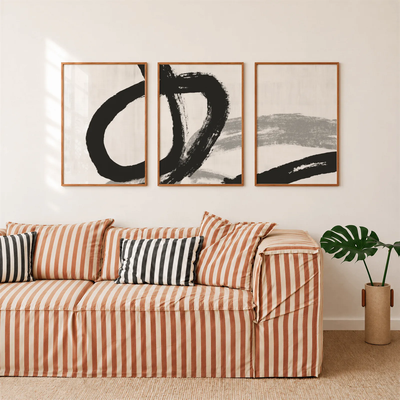 black and white minimalist brushstroke triptych wall art, above a rust-striped sofa beside a potted monstera