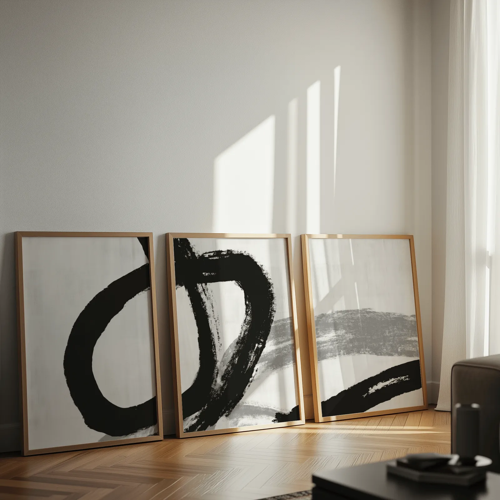 black and white minimalist brushstroke triptych wall art, leaning against a sunlit wall on herringbone flooring