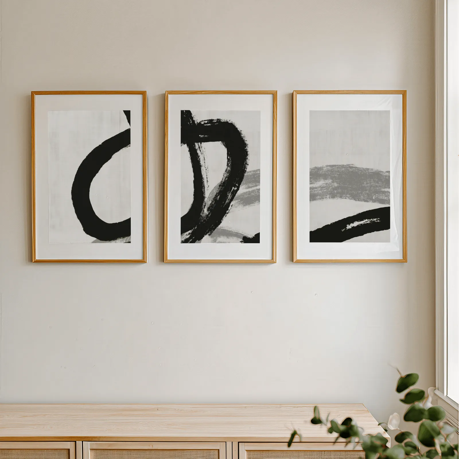 black and white minimalist brushstroke triptych wall art, in a row above a light wooden sideboard near a window