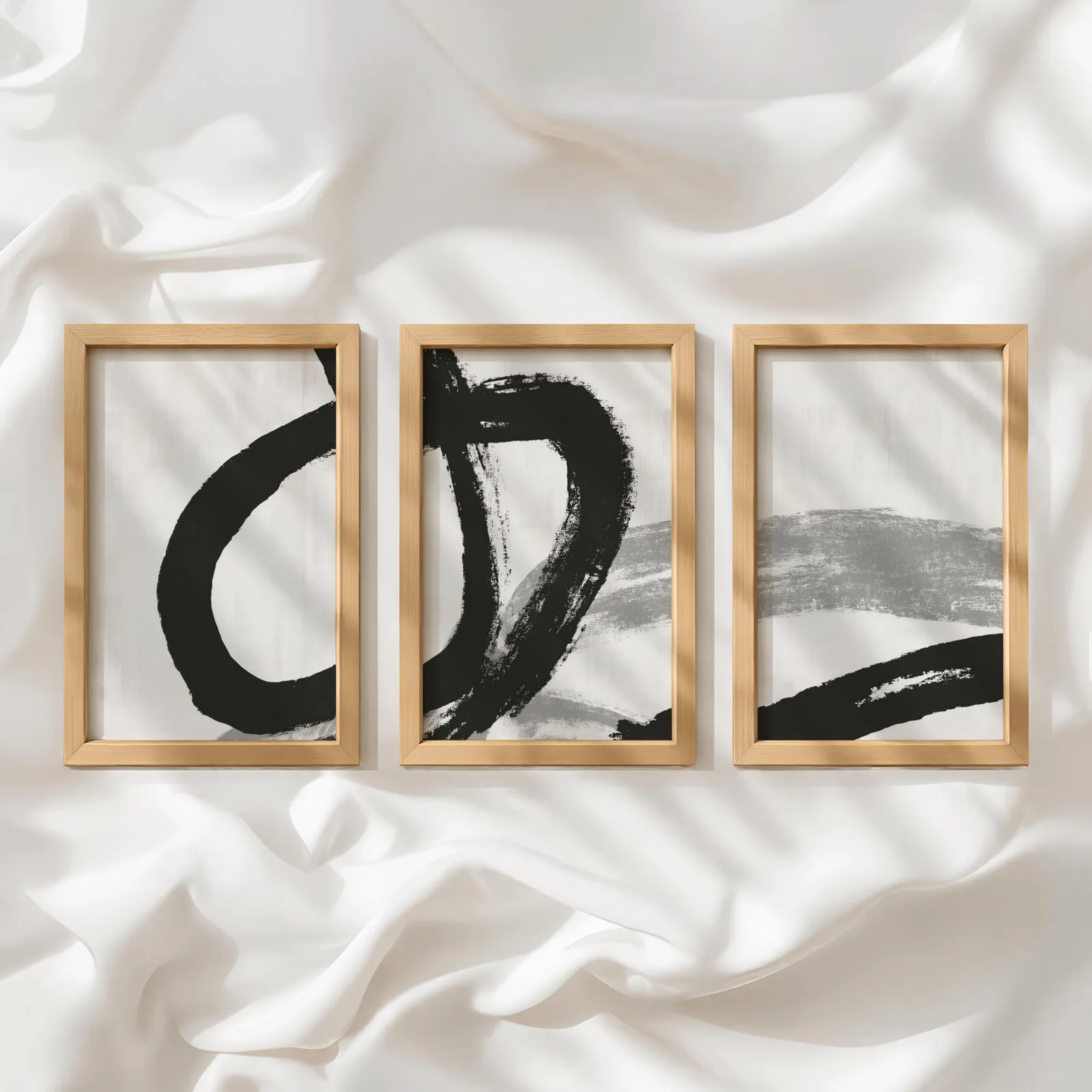black and white minimalist brushstroke triptych wall art, in a row atop rumpled white silky fabric
