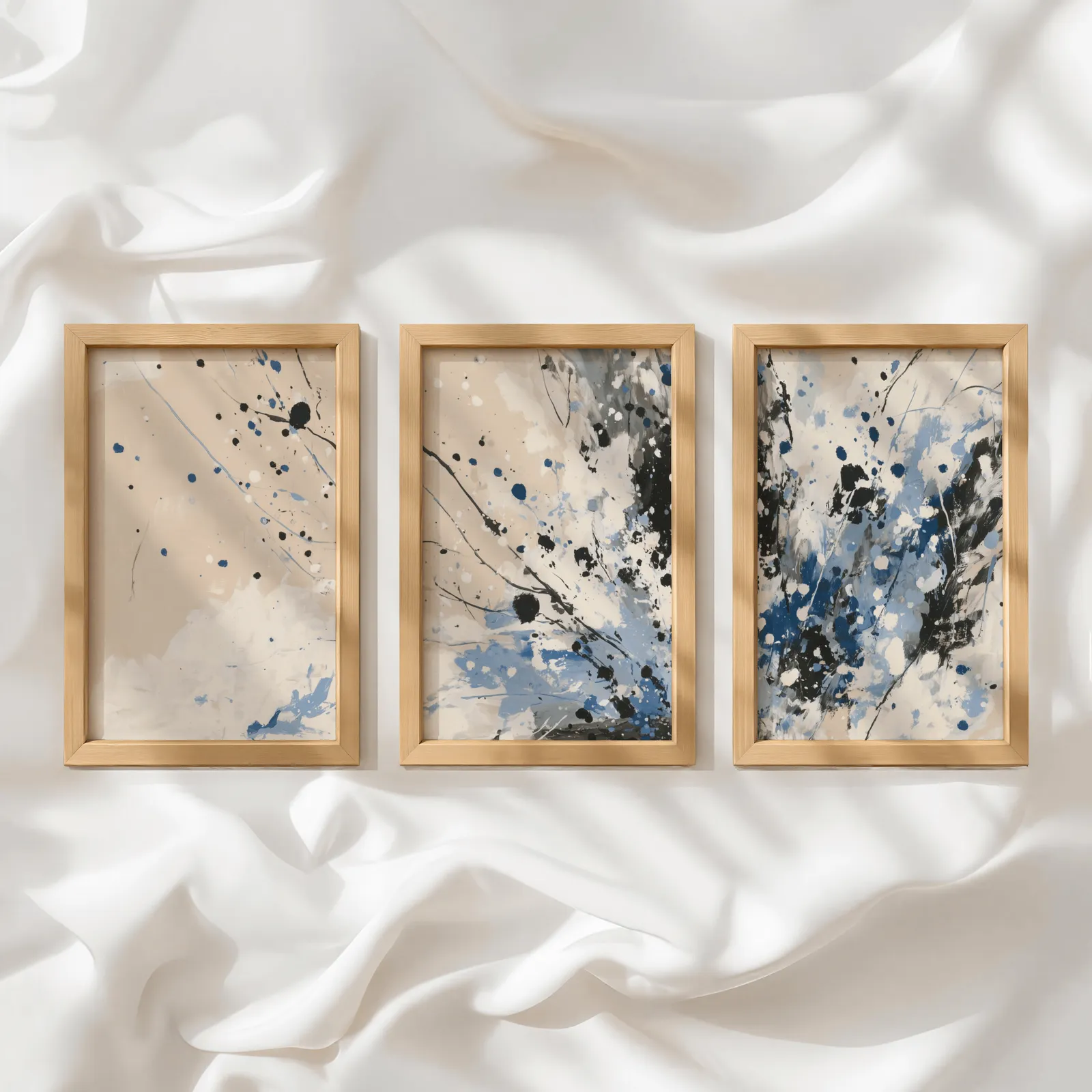 blue and beige abstract splatter triptych wall art, in a row atop rumpled white silky fabric