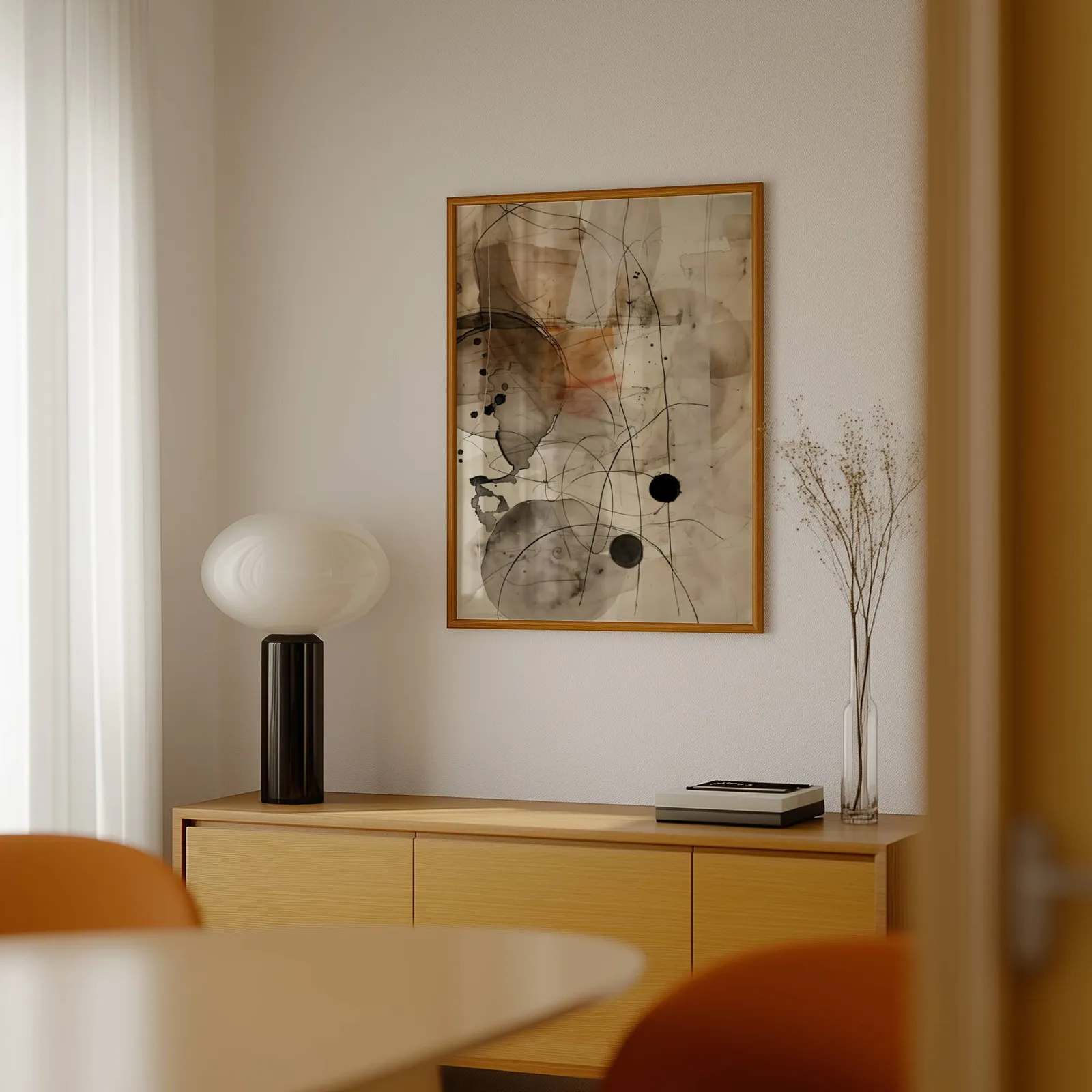abstract ink wall art in beige and black, above a light wood sideboard beside a bulbous black lamp