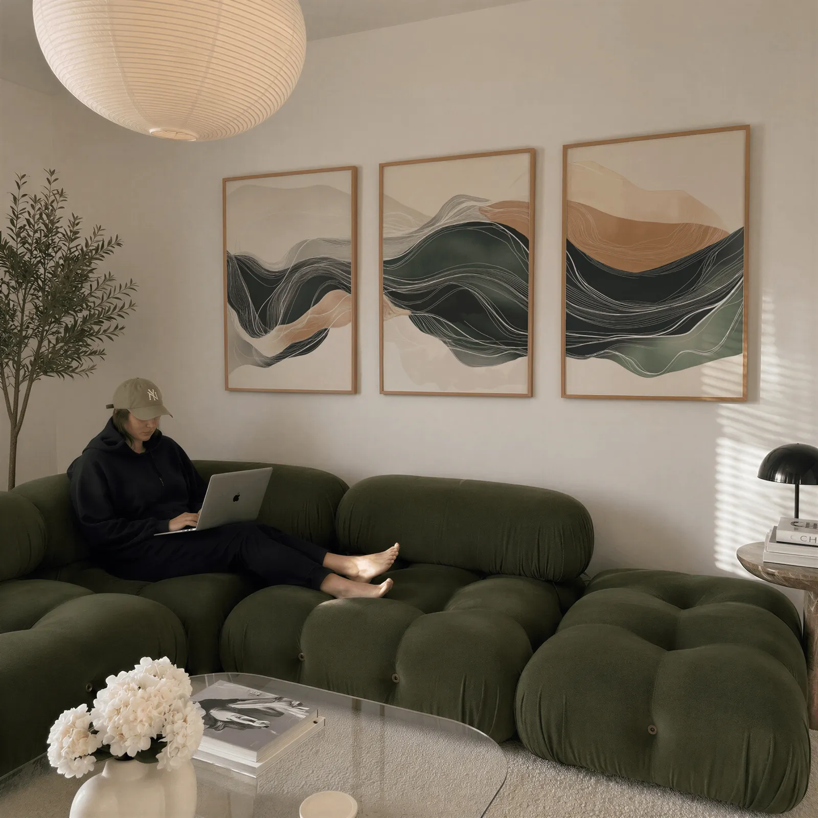 green and beige abstract landscape triptych wall art, above a plush olive velvet sectional beneath a paper lantern light