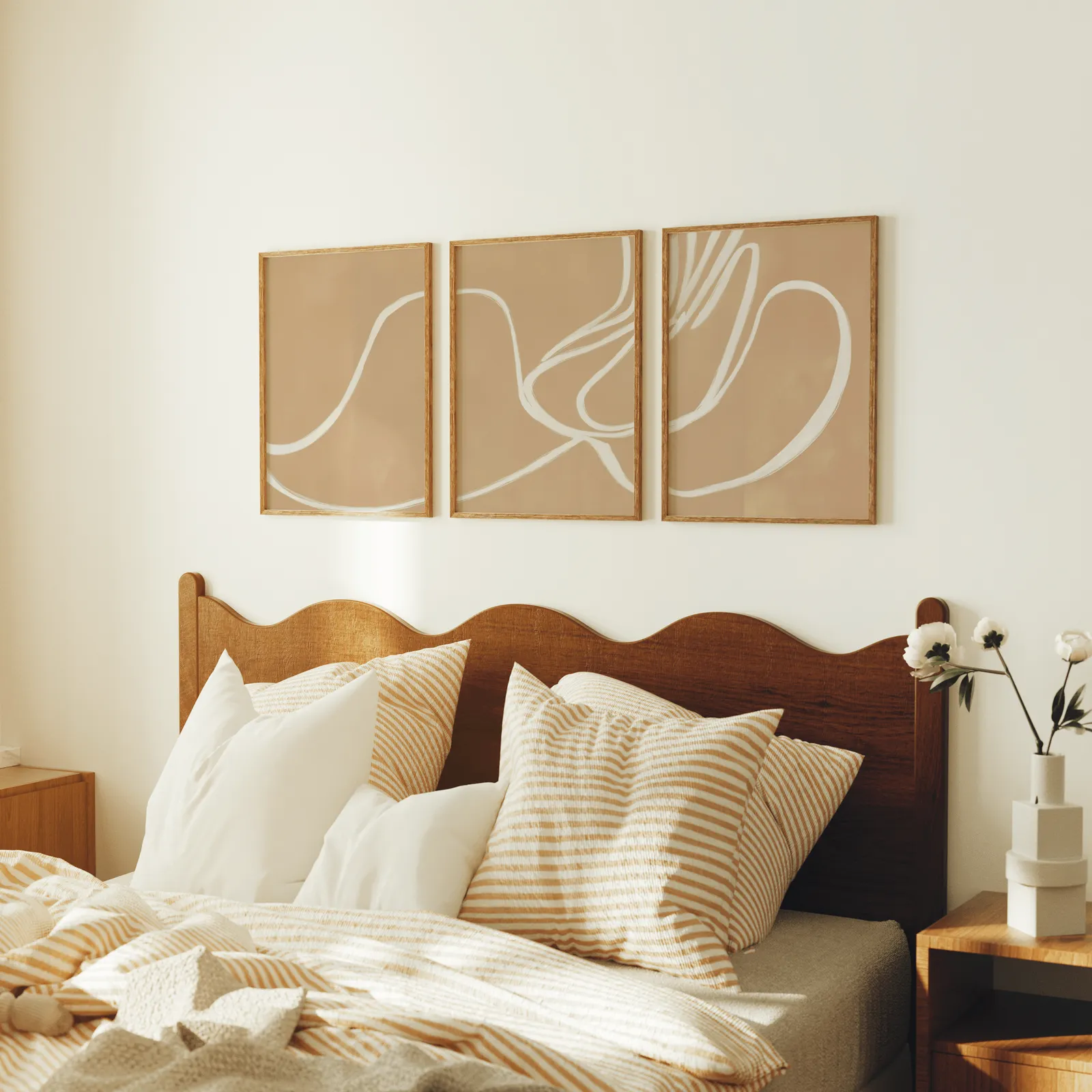 beige abstract minimalist wall art set of three, above a scalloped wooden headboard with striped pillows