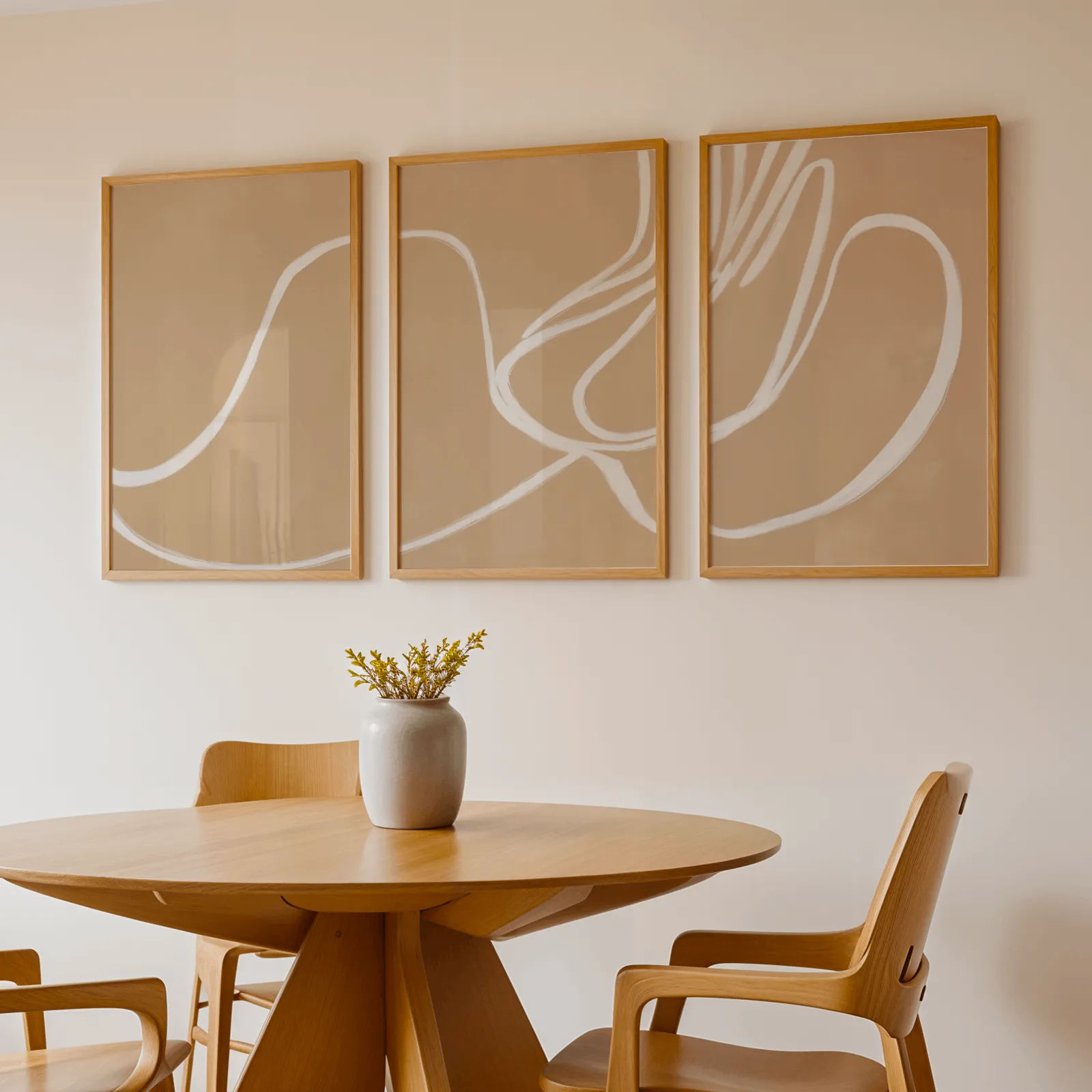 beige abstract minimalist wall art set of three, above a round wooden table with a stoneware vase