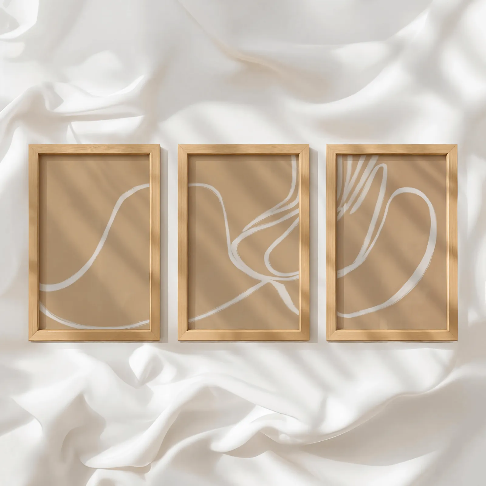 beige abstract minimalist wall art set of three, in a row atop rumpled white silky fabric