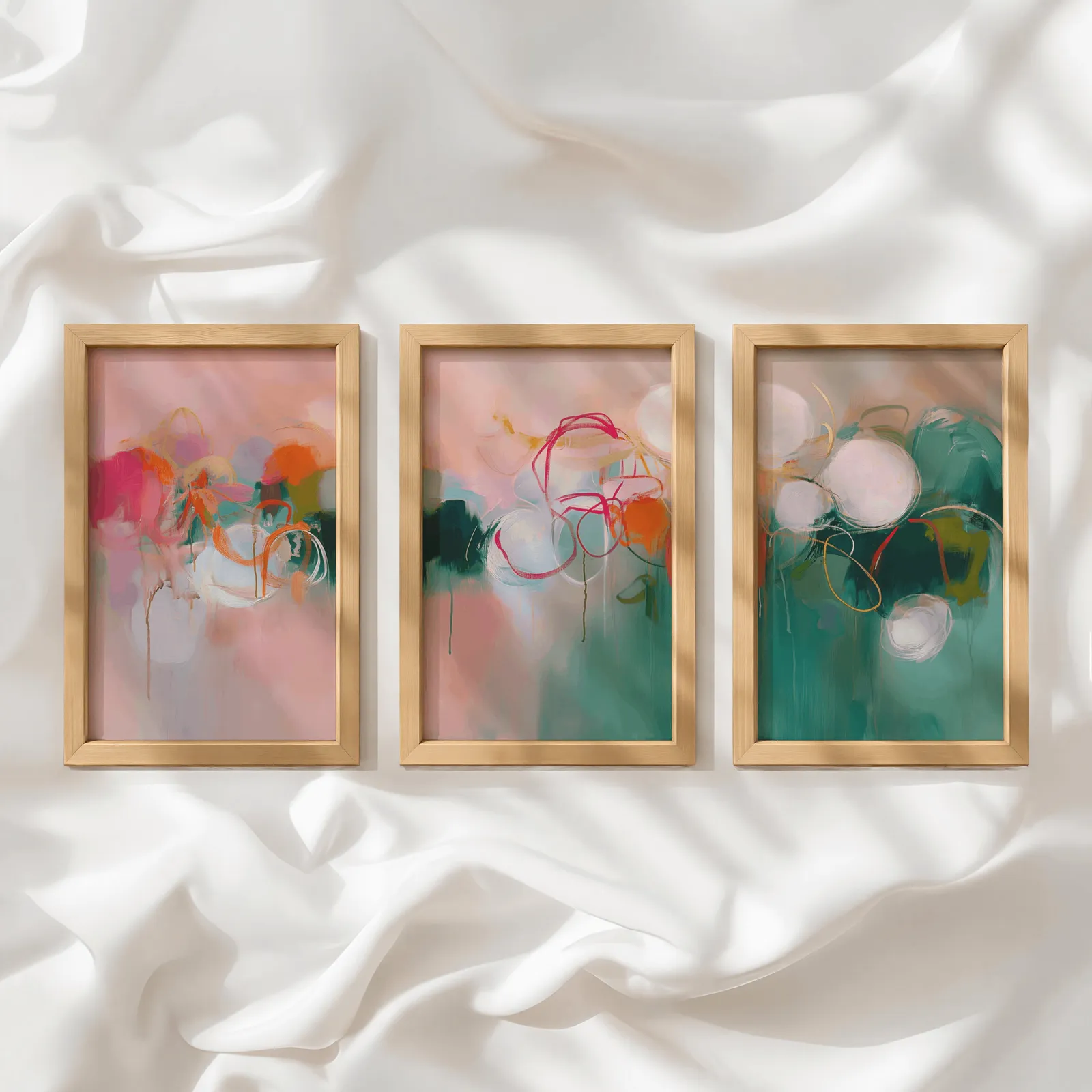 colorful abstract triptych wall art in pink and green, in a row atop rumpled white silky fabric
