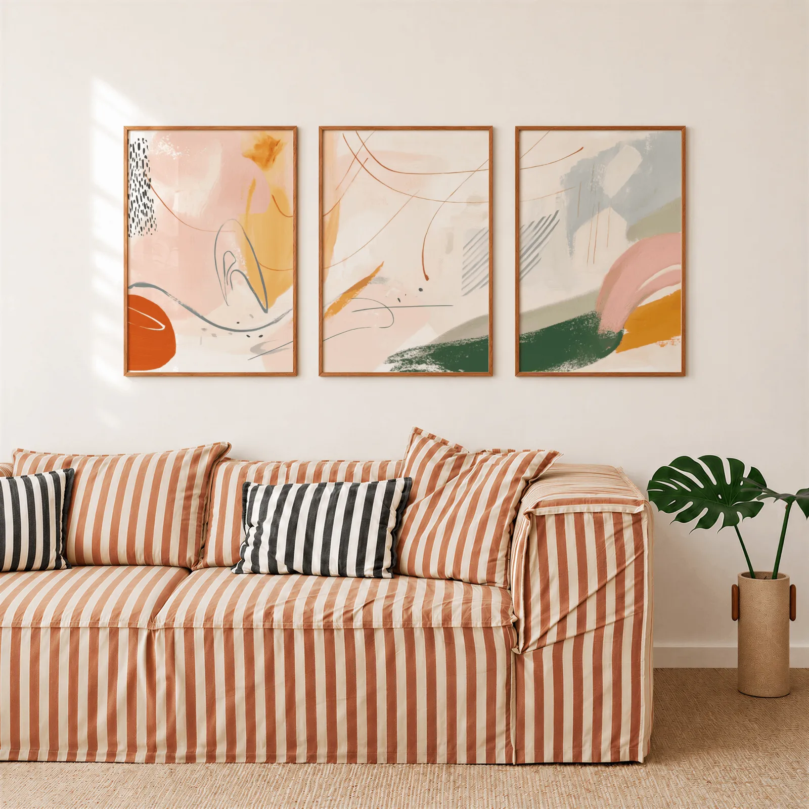 colorful abstract wall art set of three, above a rust-striped sofa beside a potted monstera