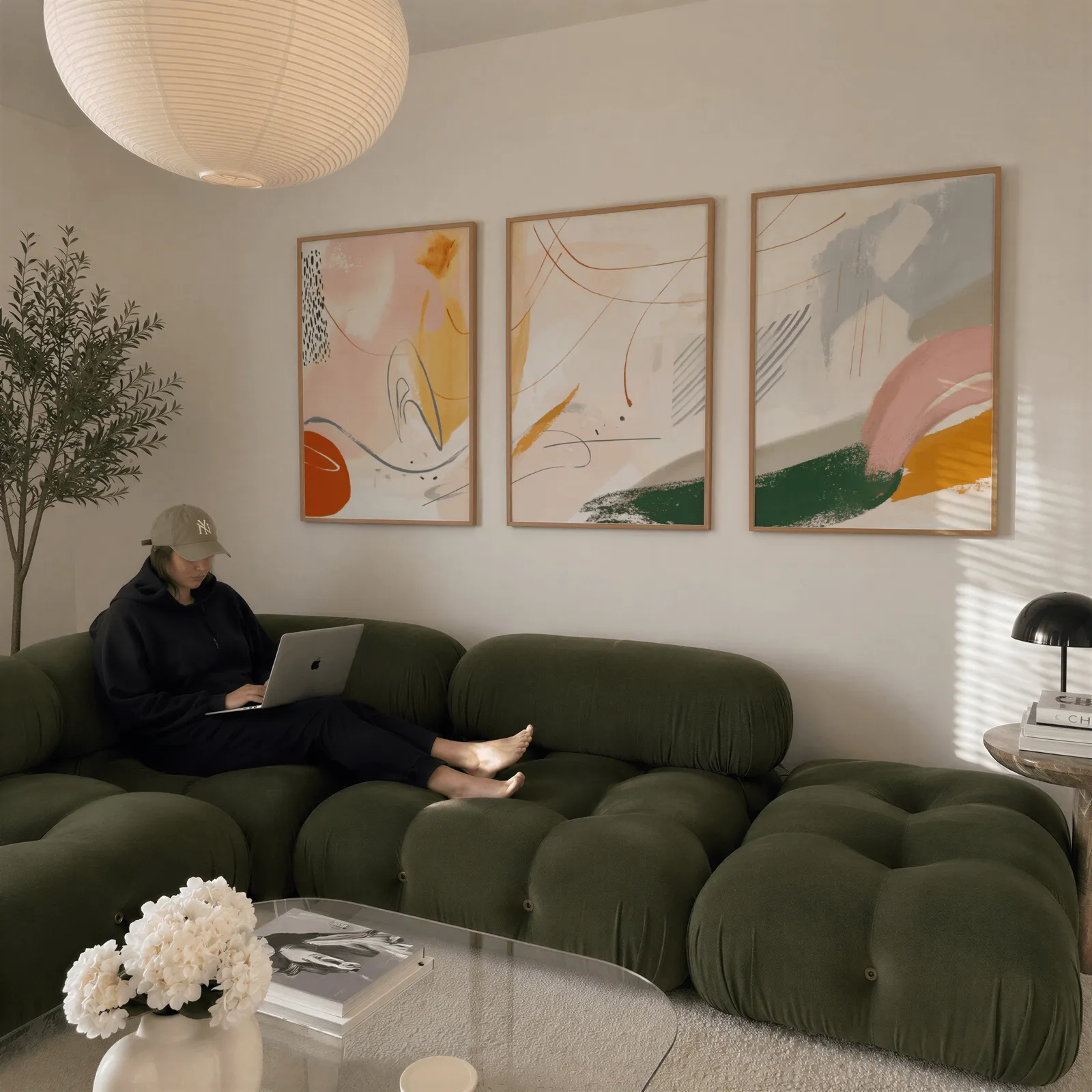 colorful abstract wall art set of three, above a plush olive velvet sectional beneath a paper lantern light