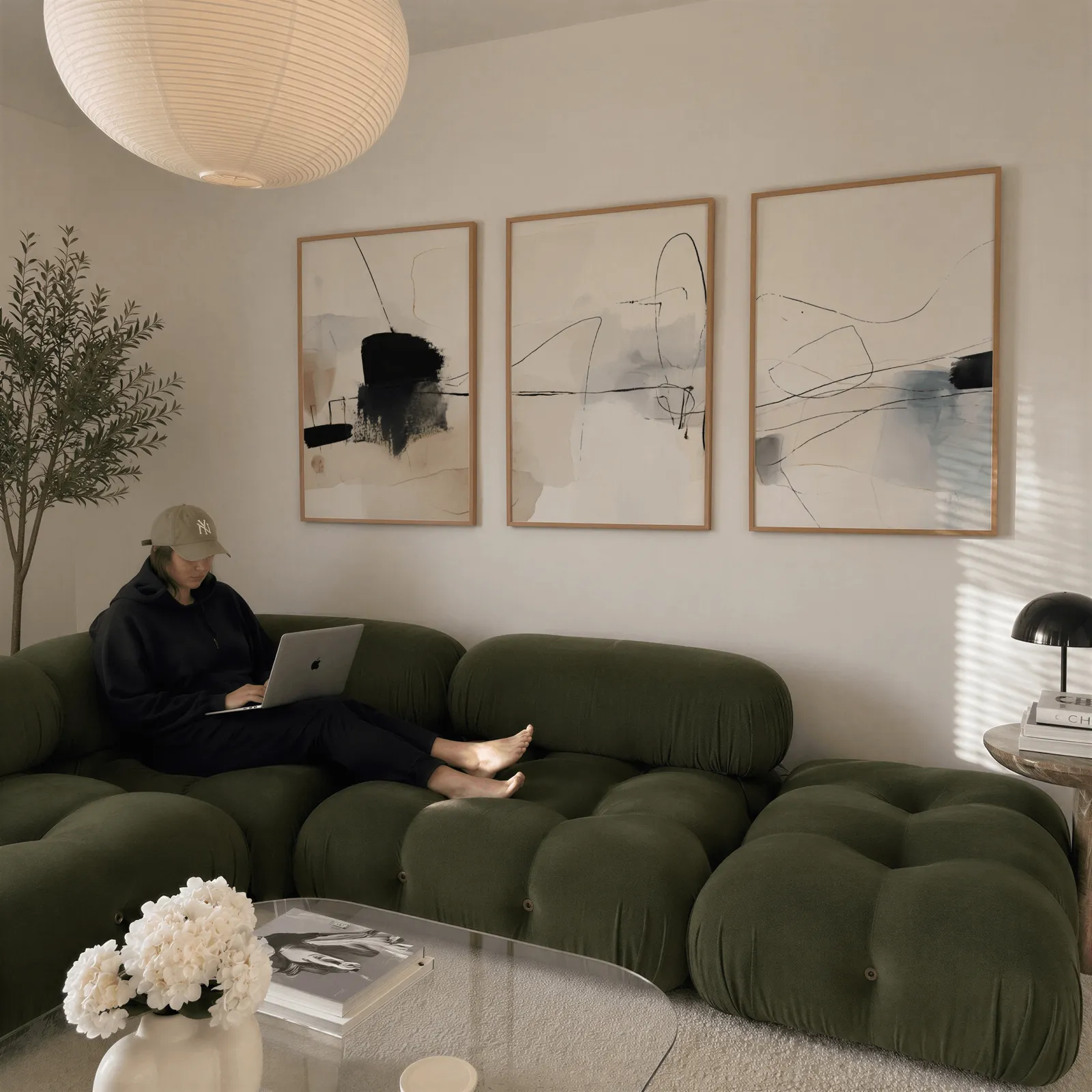 neutral abstract minimalist wall art set of three, above a plush olive velvet sectional beneath a paper lantern light