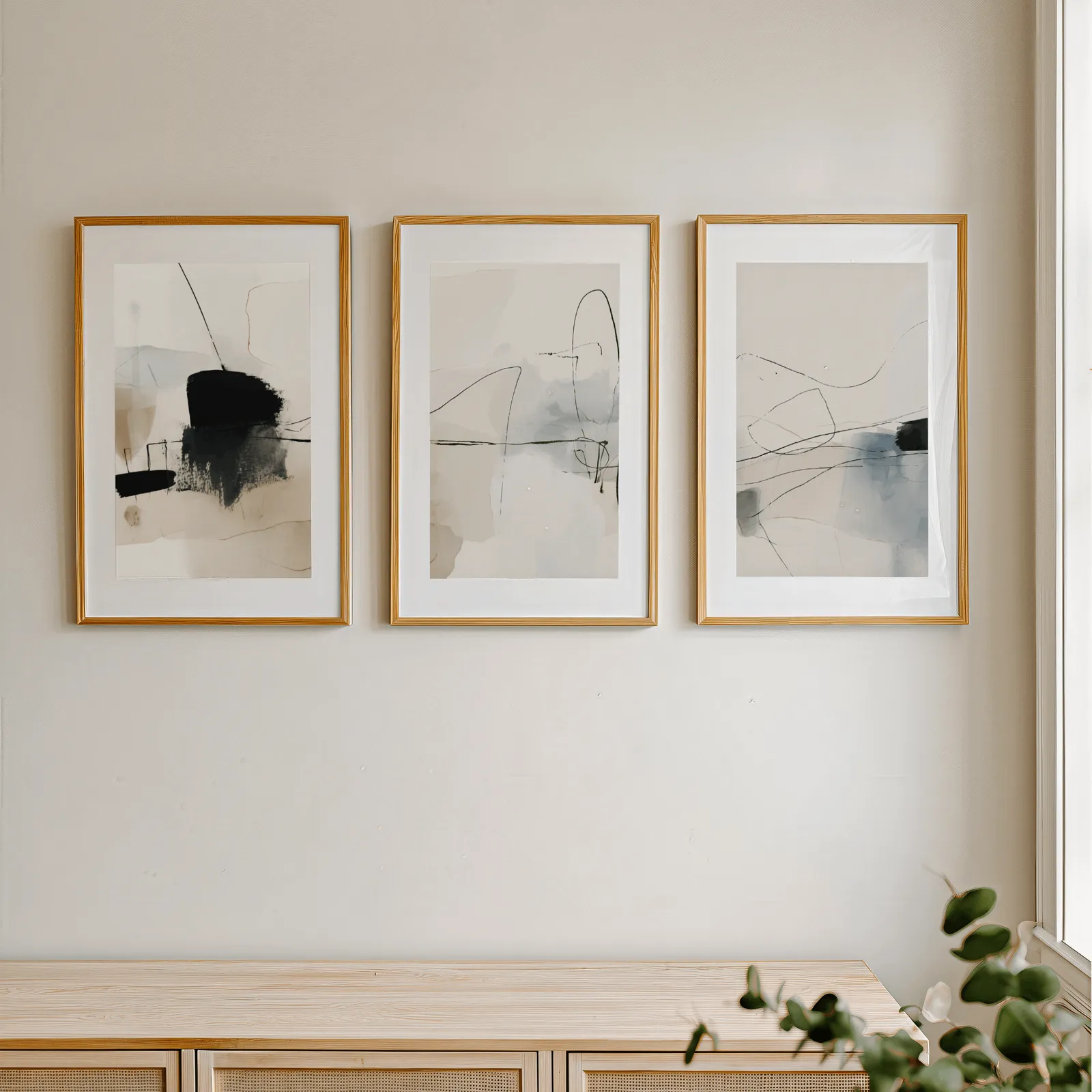 neutral abstract minimalist wall art set of three, in a row above a light wooden sideboard near a window
