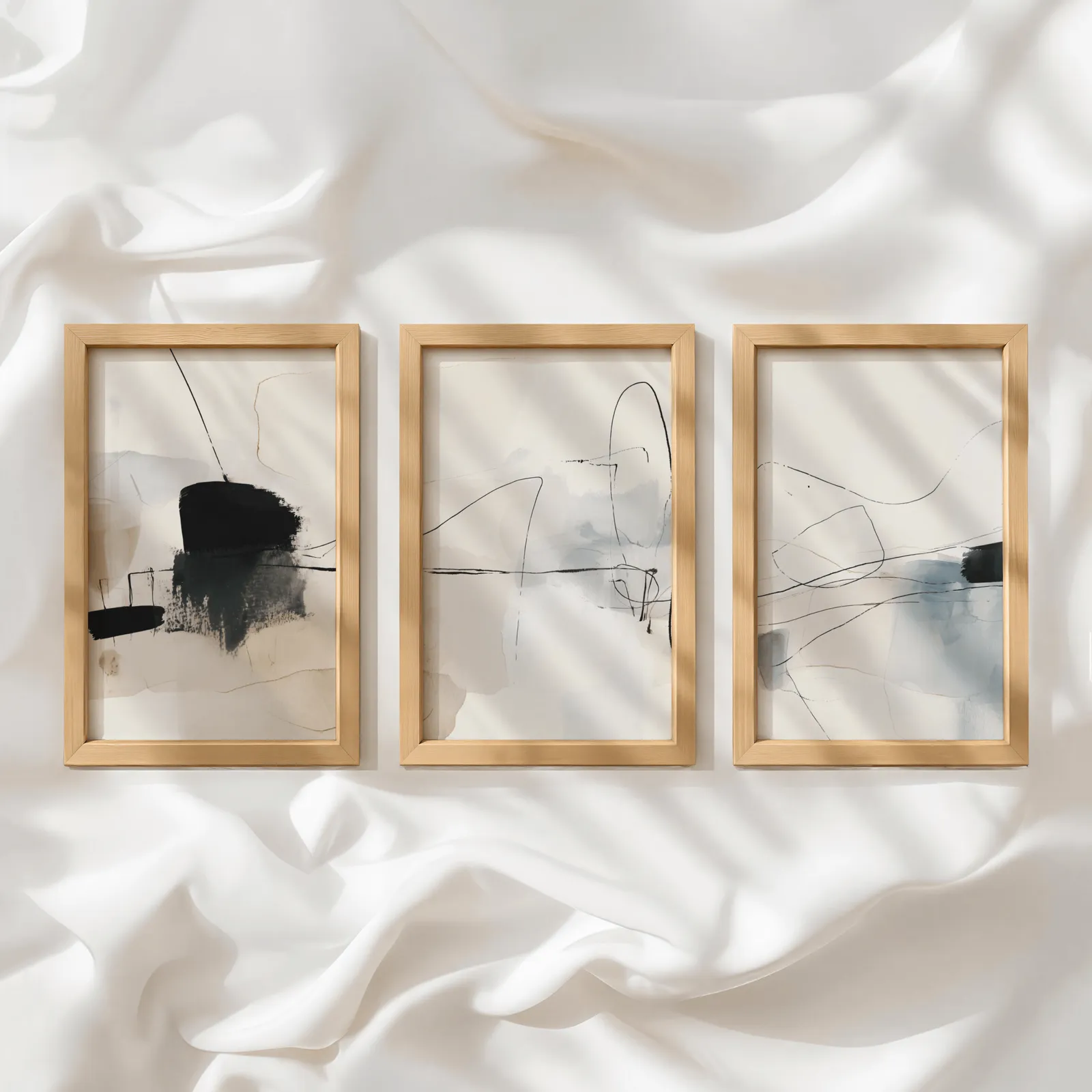 neutral abstract minimalist wall art set of three, in a row atop rumpled white silky fabric
