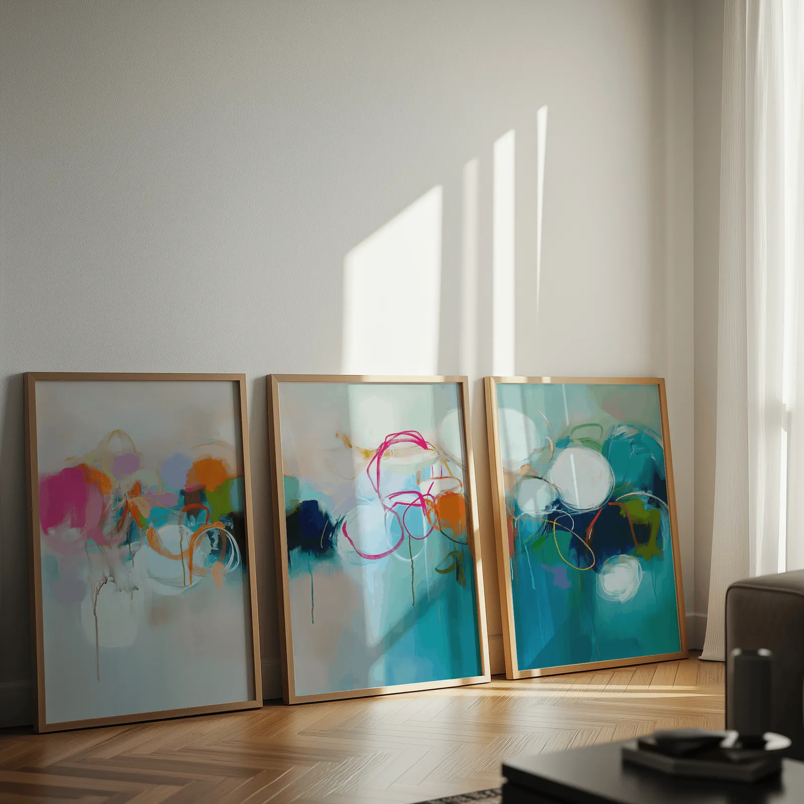 colorful abstract triptych wall art in teal and pink, leaning against a sunlit wall on herringbone flooring