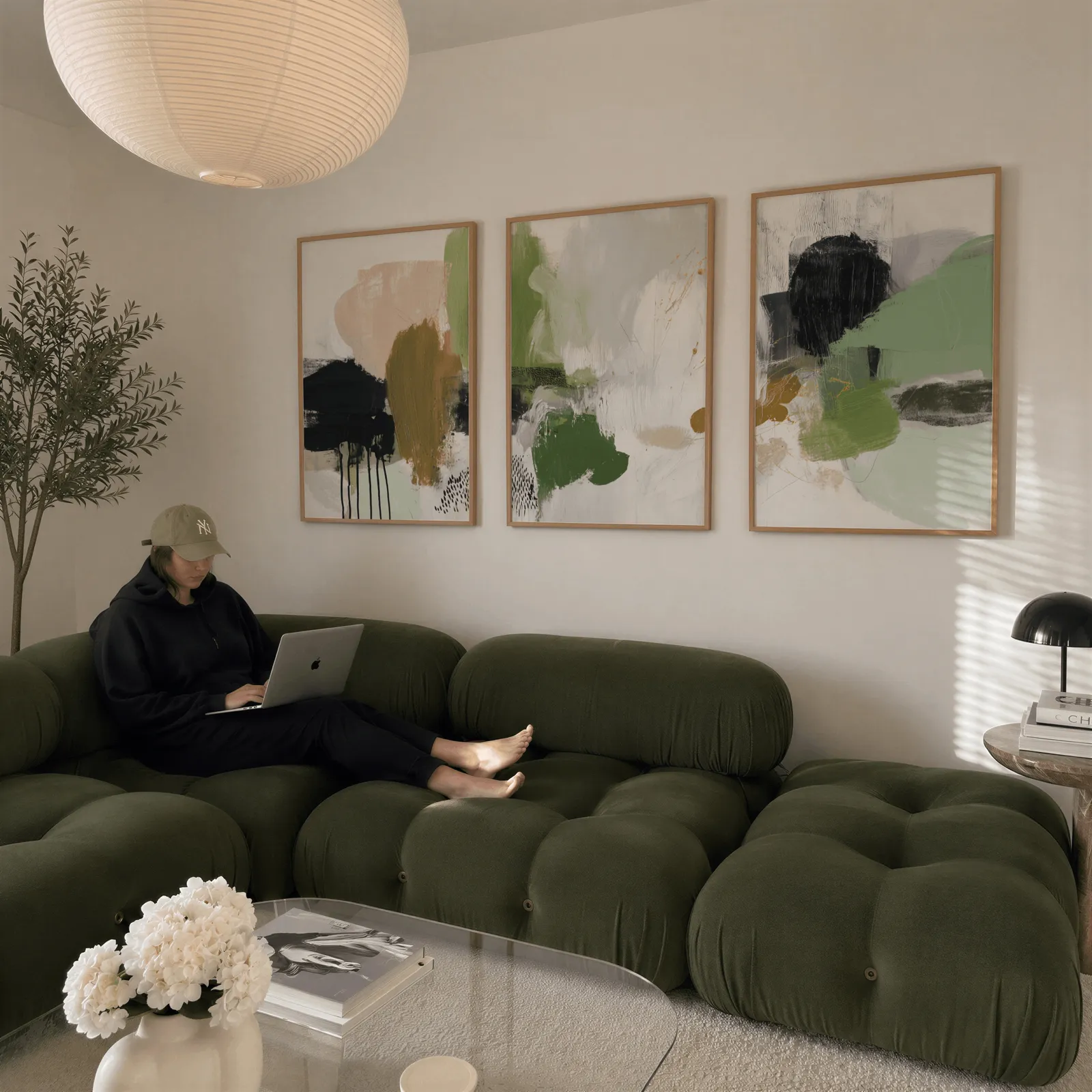 green and blush abstract wall art set of 3, above a plush olive velvet sectional beneath a paper lantern light
