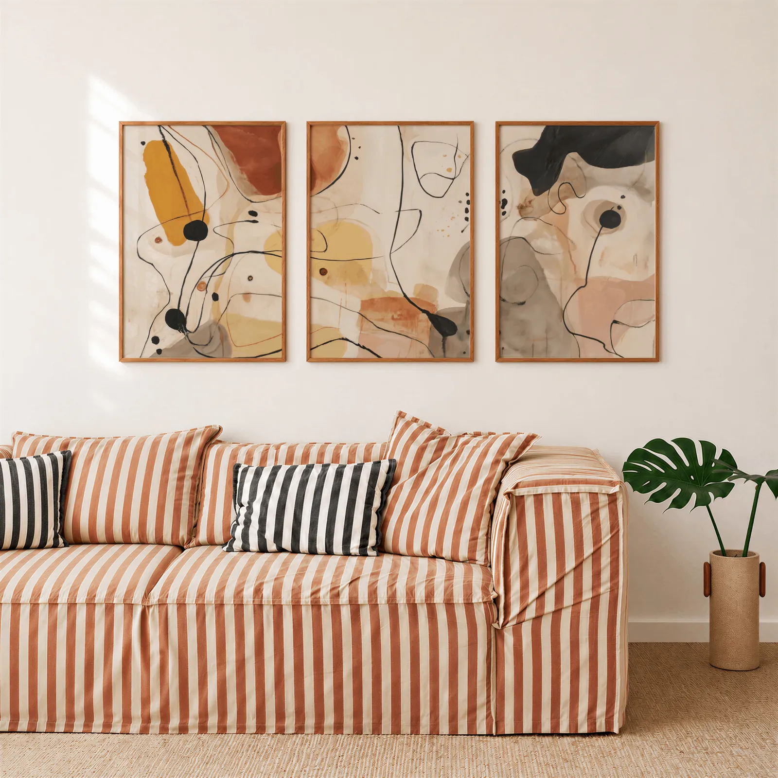 terracotta abstract line art set of three, above a rust-striped sofa beside a potted monstera