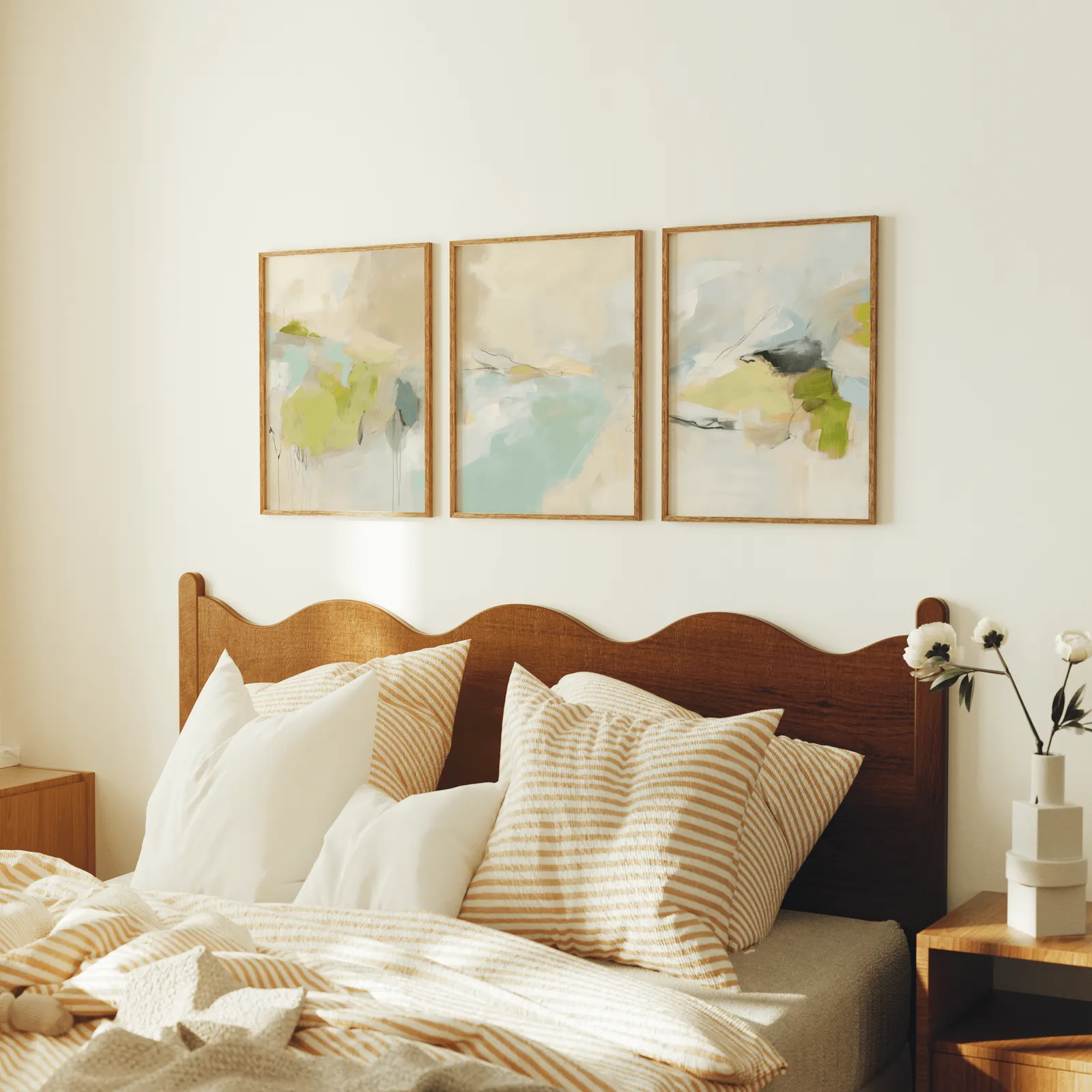 green and beige abstract wall art set of 3, above a scalloped wooden headboard with striped pillows
