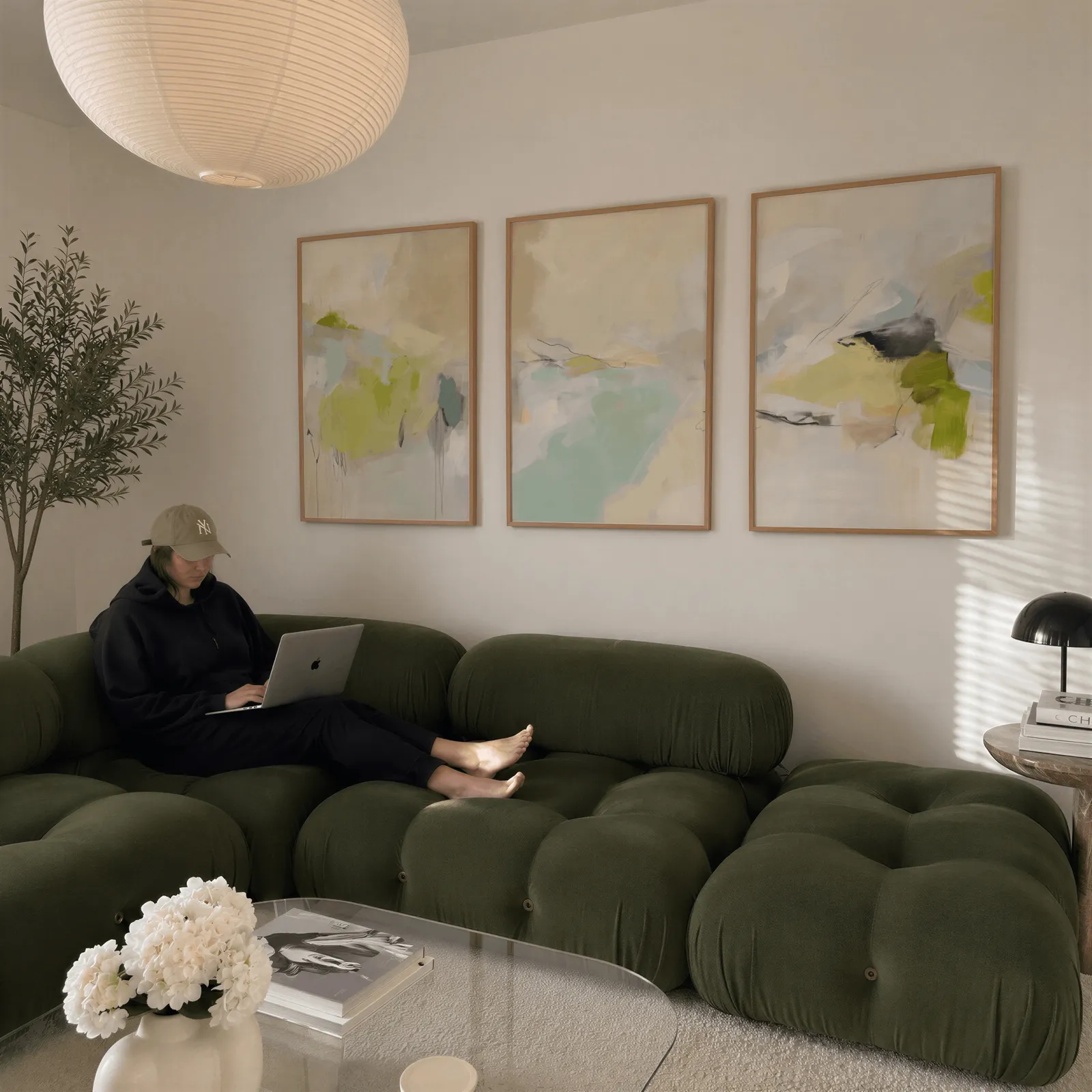 green and beige abstract wall art set of 3, above a plush olive velvet sectional beneath a paper lantern light
