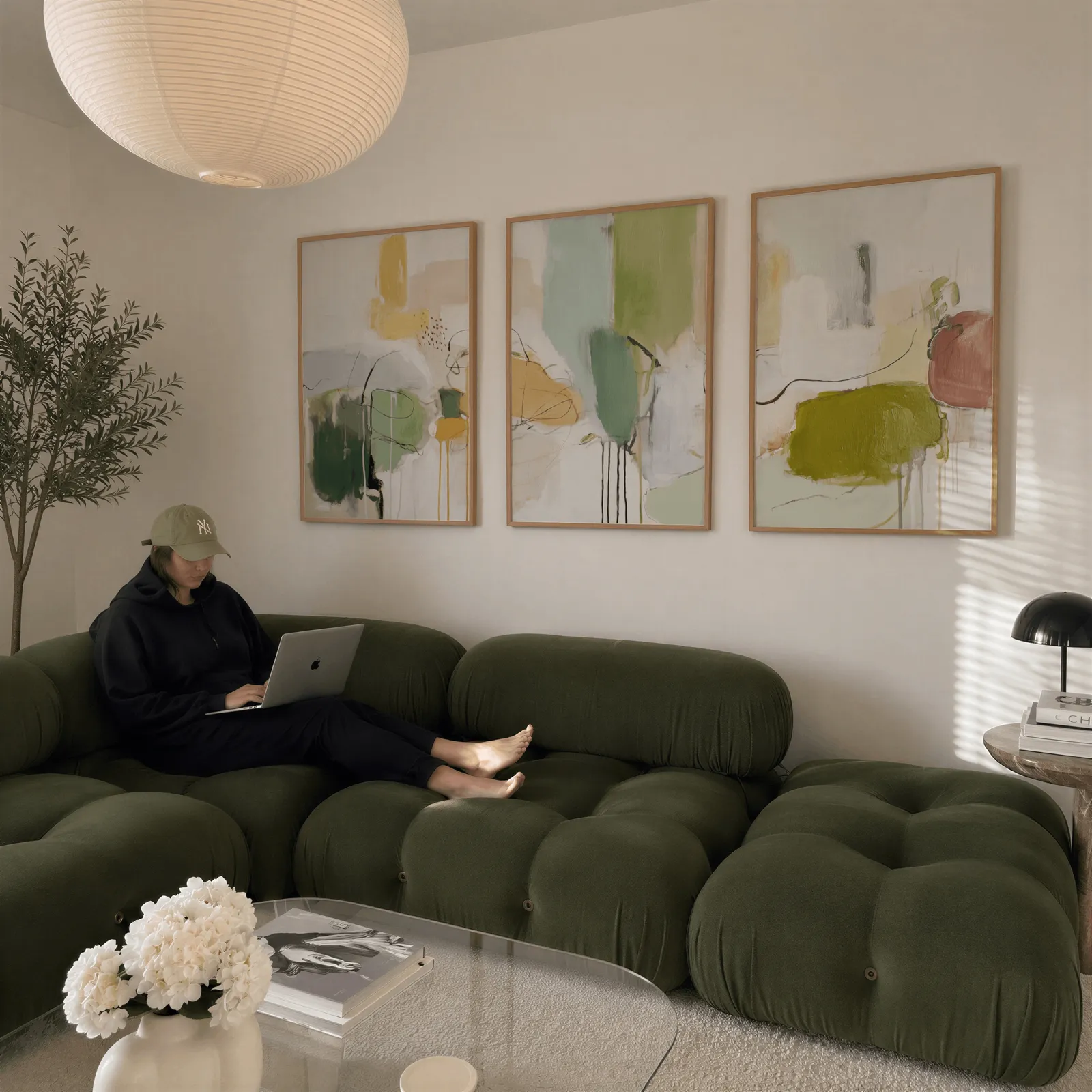 green abstract set of 3 wall art panels, above a plush olive velvet sectional beneath a paper lantern light