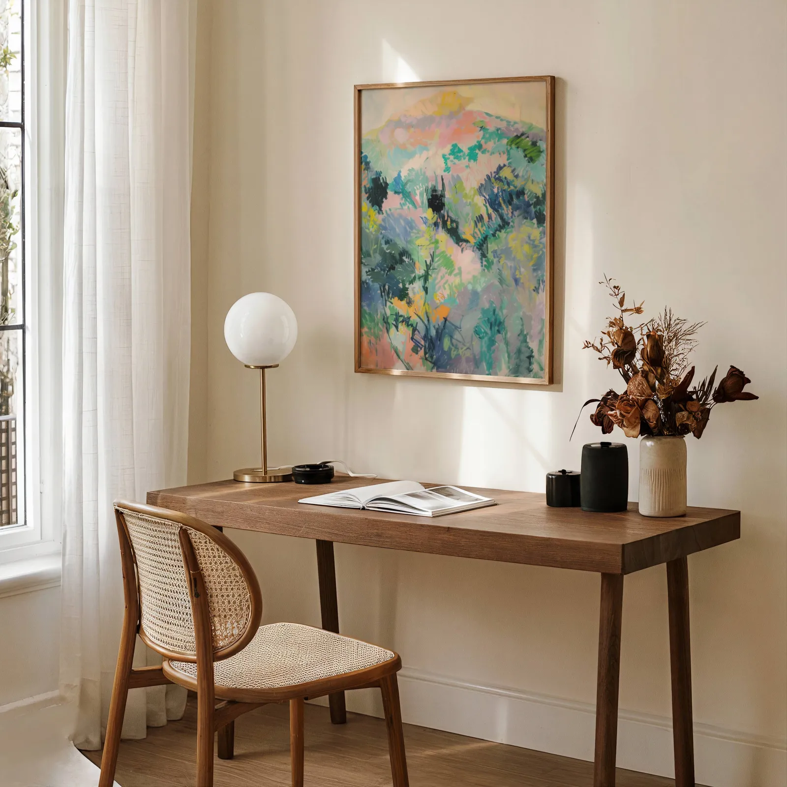colorful landscape wall art of hillside foliage, above a wooden desk with a globe lamp and dried flowers