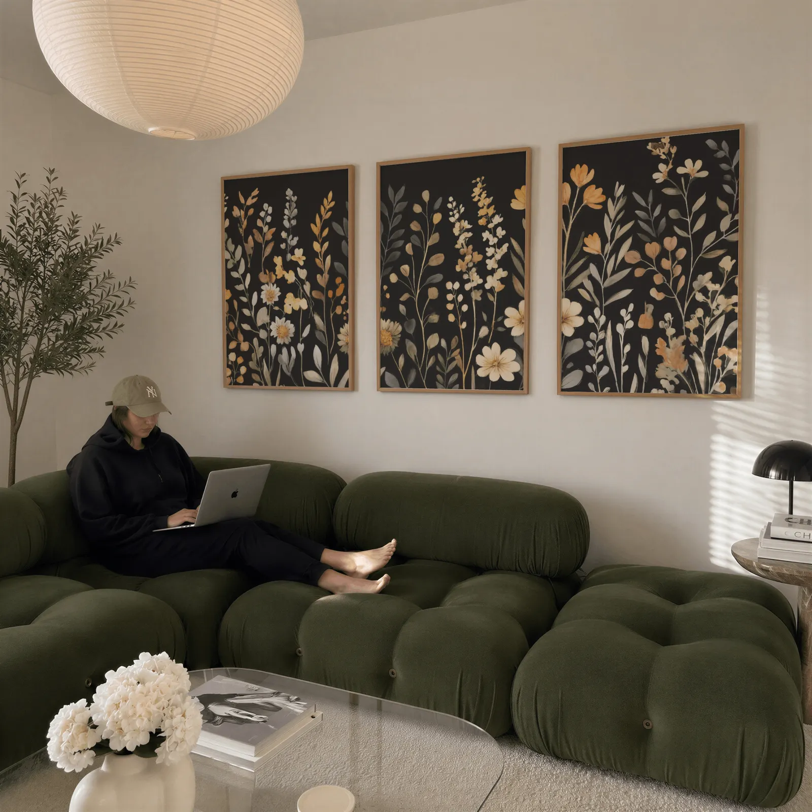 black botanical wildflower wall art set of 3, above a plush olive velvet sectional beneath a paper lantern light