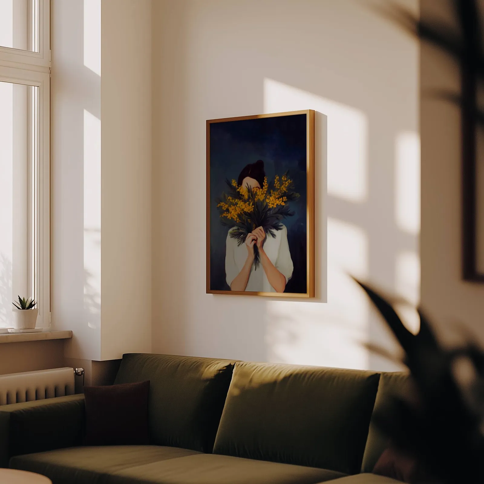 woman with yellow mimosa flowers wall art, above an olive velvet sofa in raking afternoon light