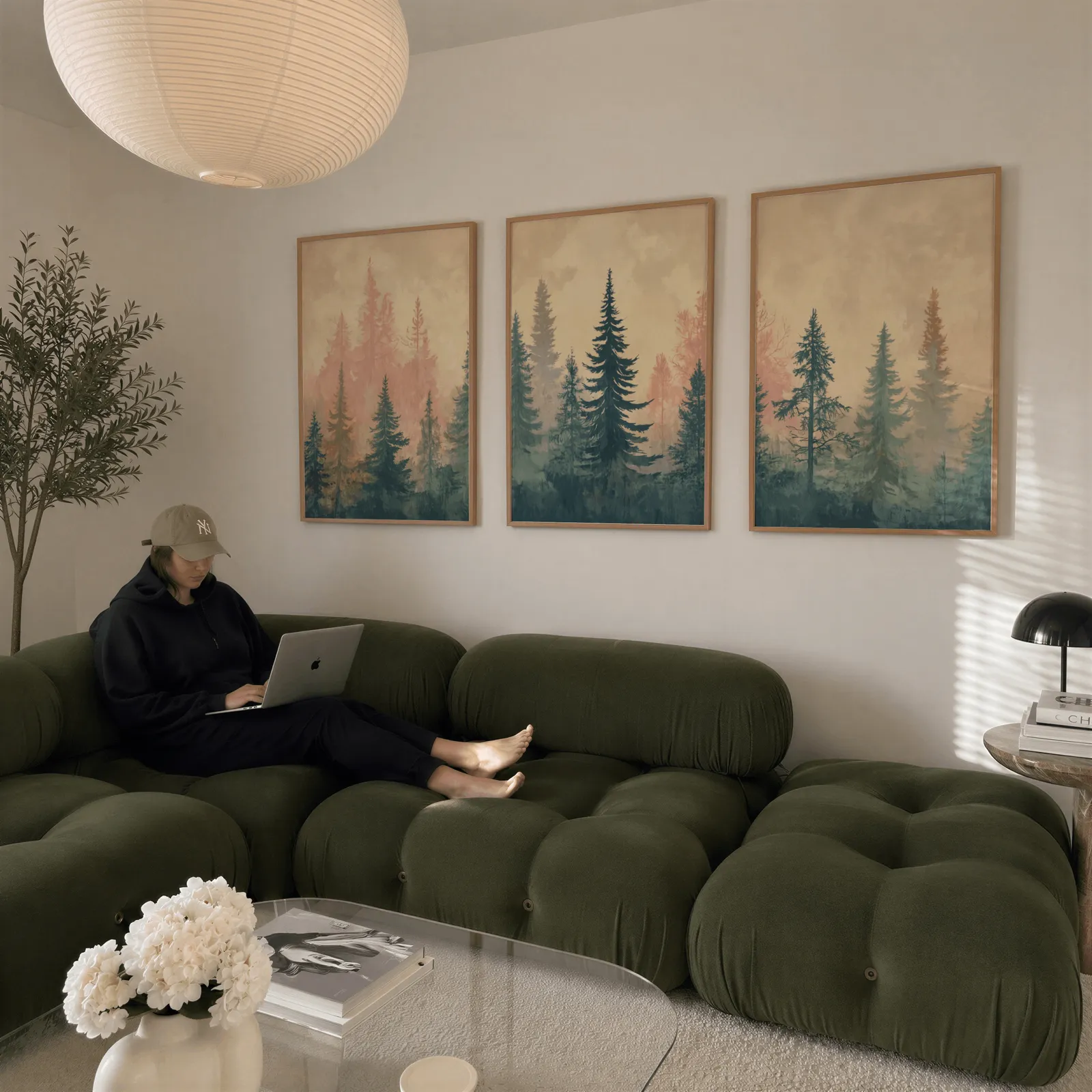 misty forest triptych wall art in pink and blue, above a plush olive velvet sectional beneath a paper lantern light