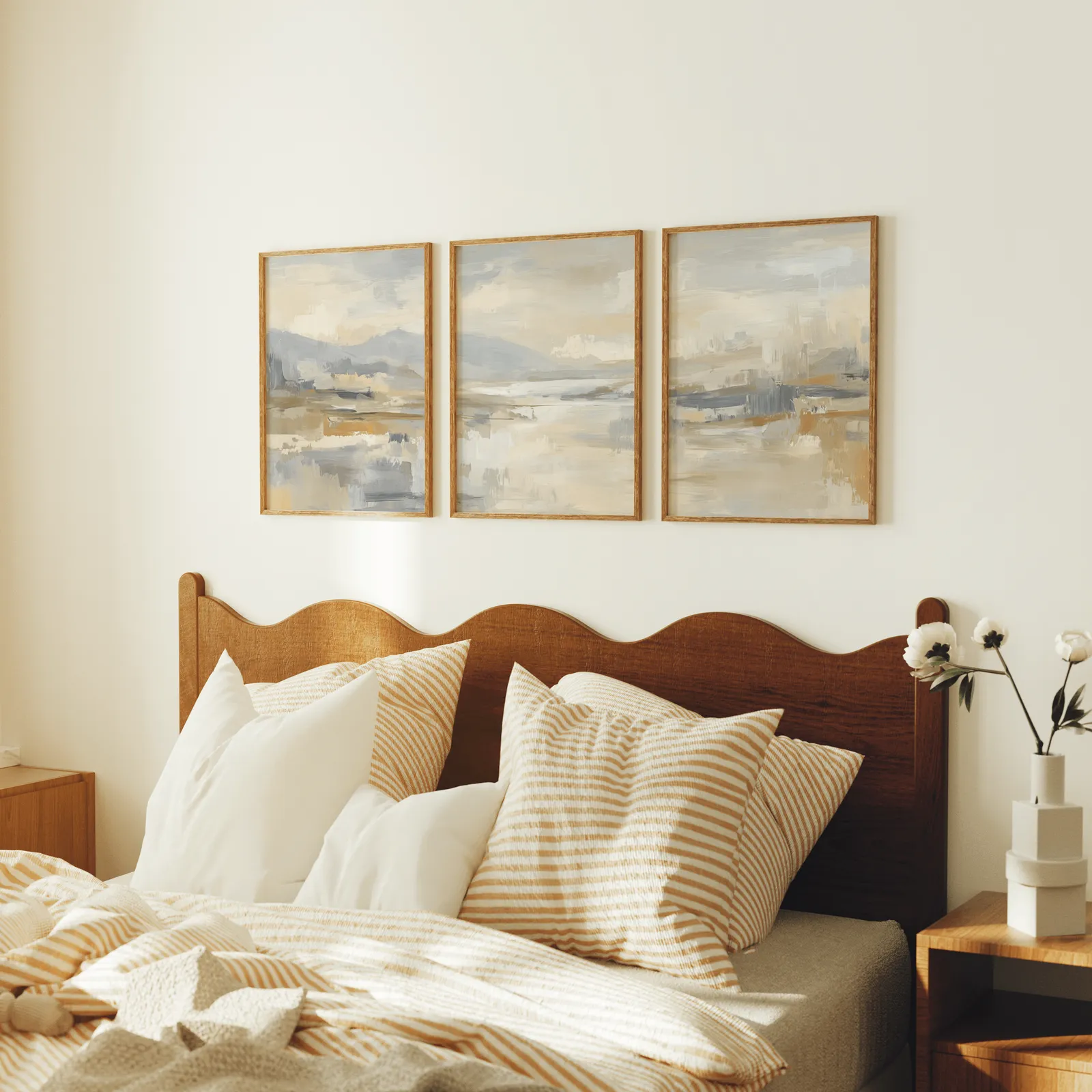 neutral abstract landscape wall art set of three, above a scalloped wooden headboard with striped pillows
