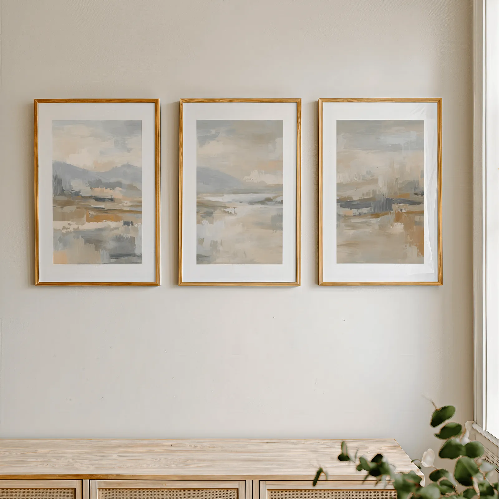 neutral abstract landscape wall art set of three, in a row above a light wooden sideboard near a window