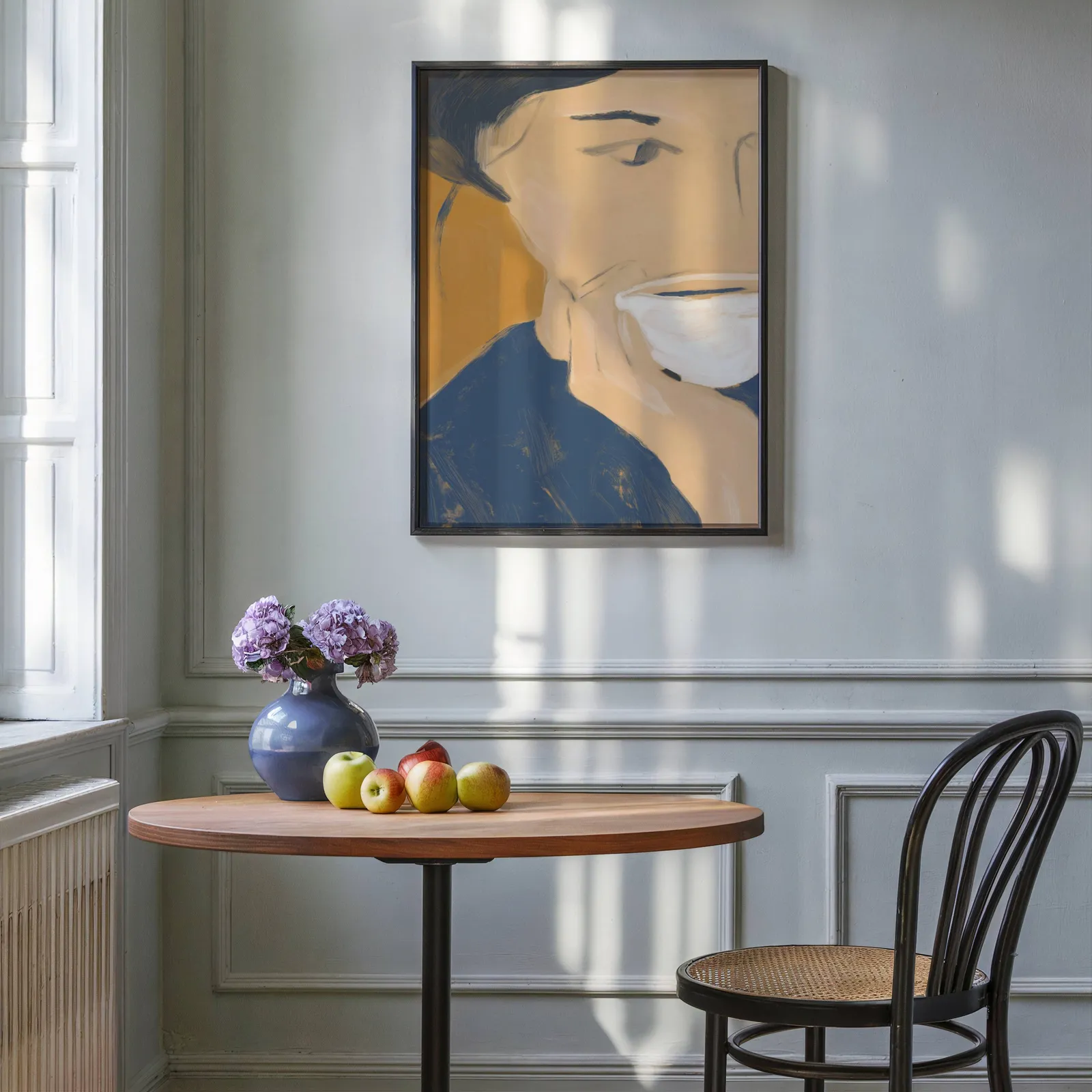 abstract portrait wall art with teacup in blue and orange, above a round wooden table with apples and a blue vase