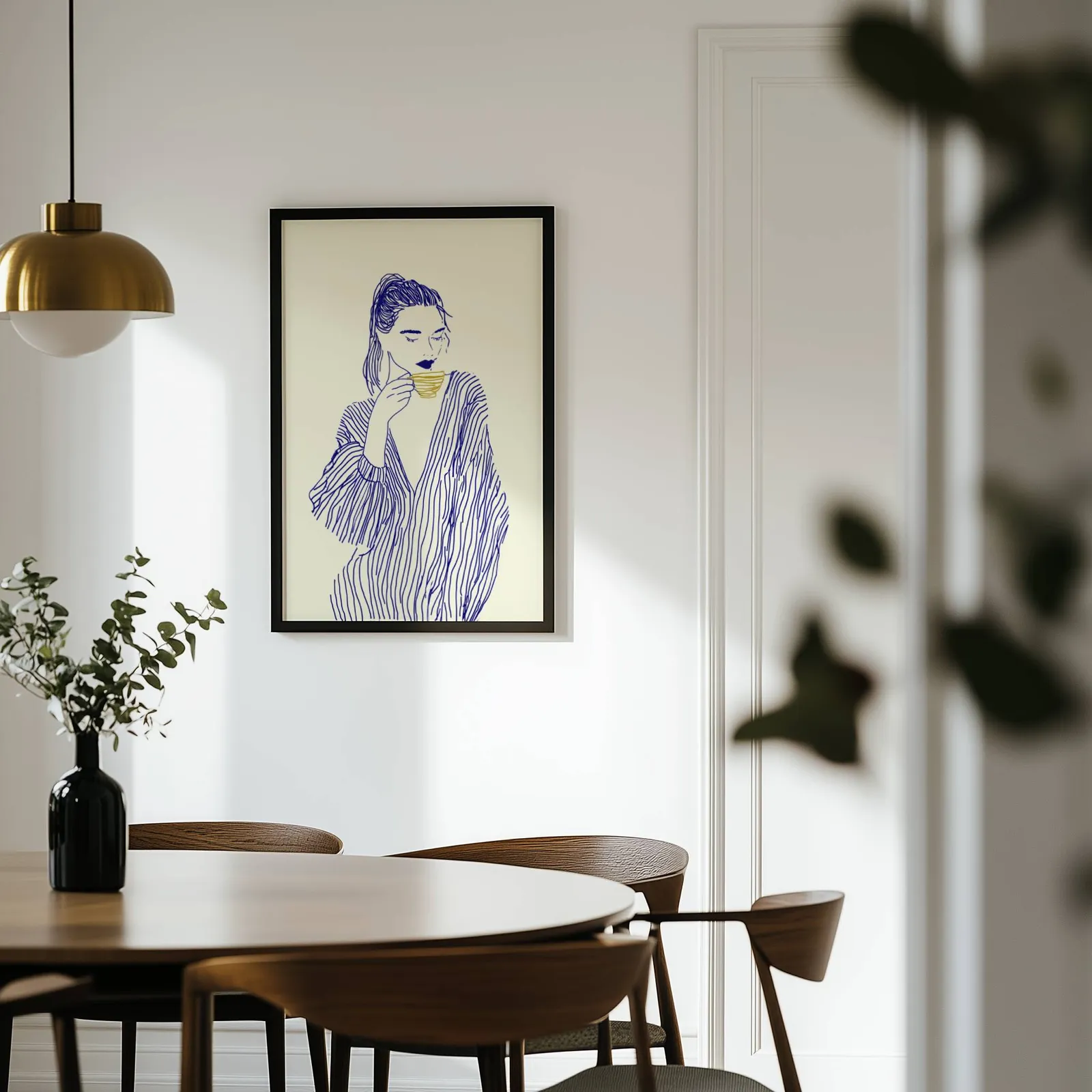 blue line art woman drinking coffee minimalist print, on a white wall above a round wooden dining table
