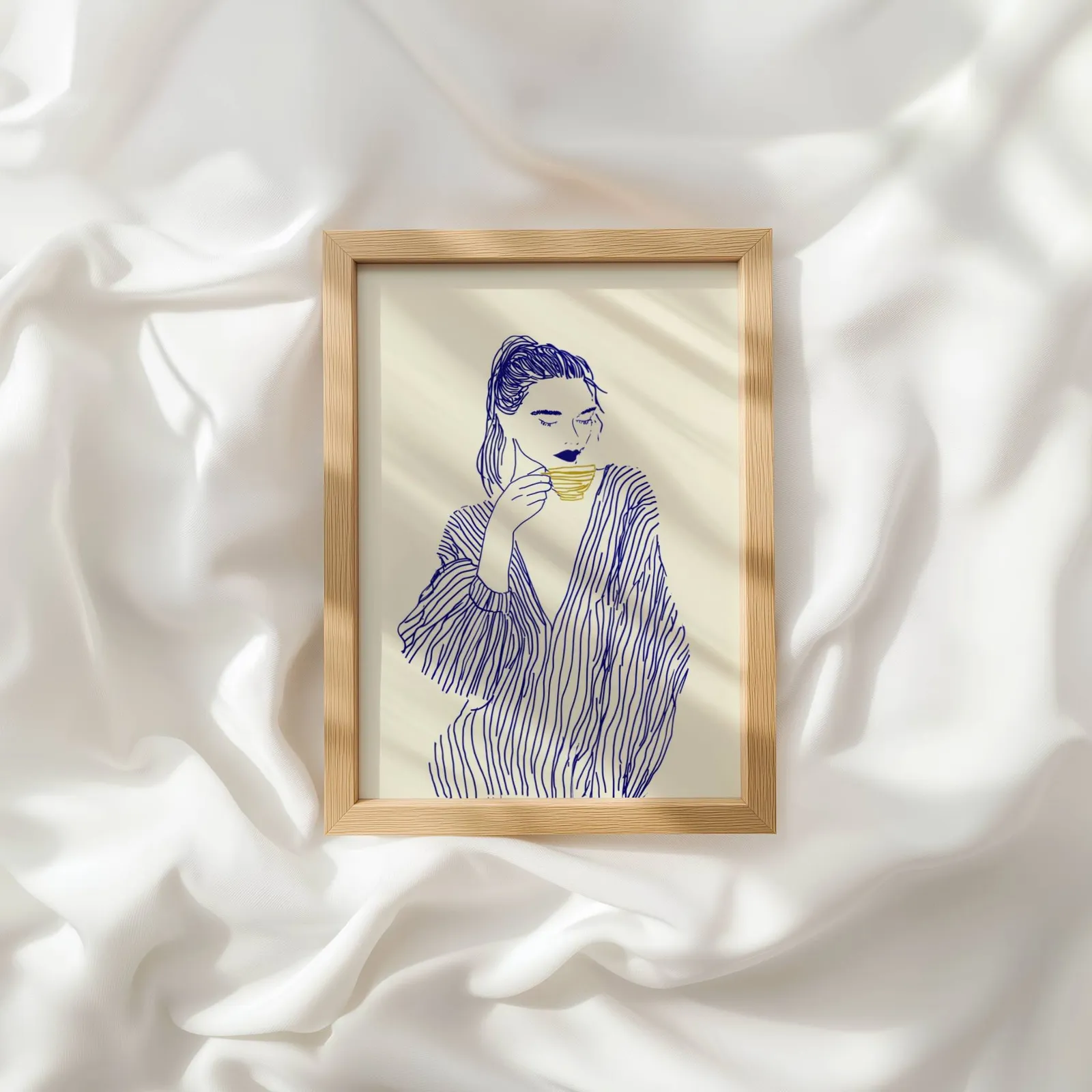 blue line art woman drinking coffee minimalist print, resting atop rumpled white silky fabric