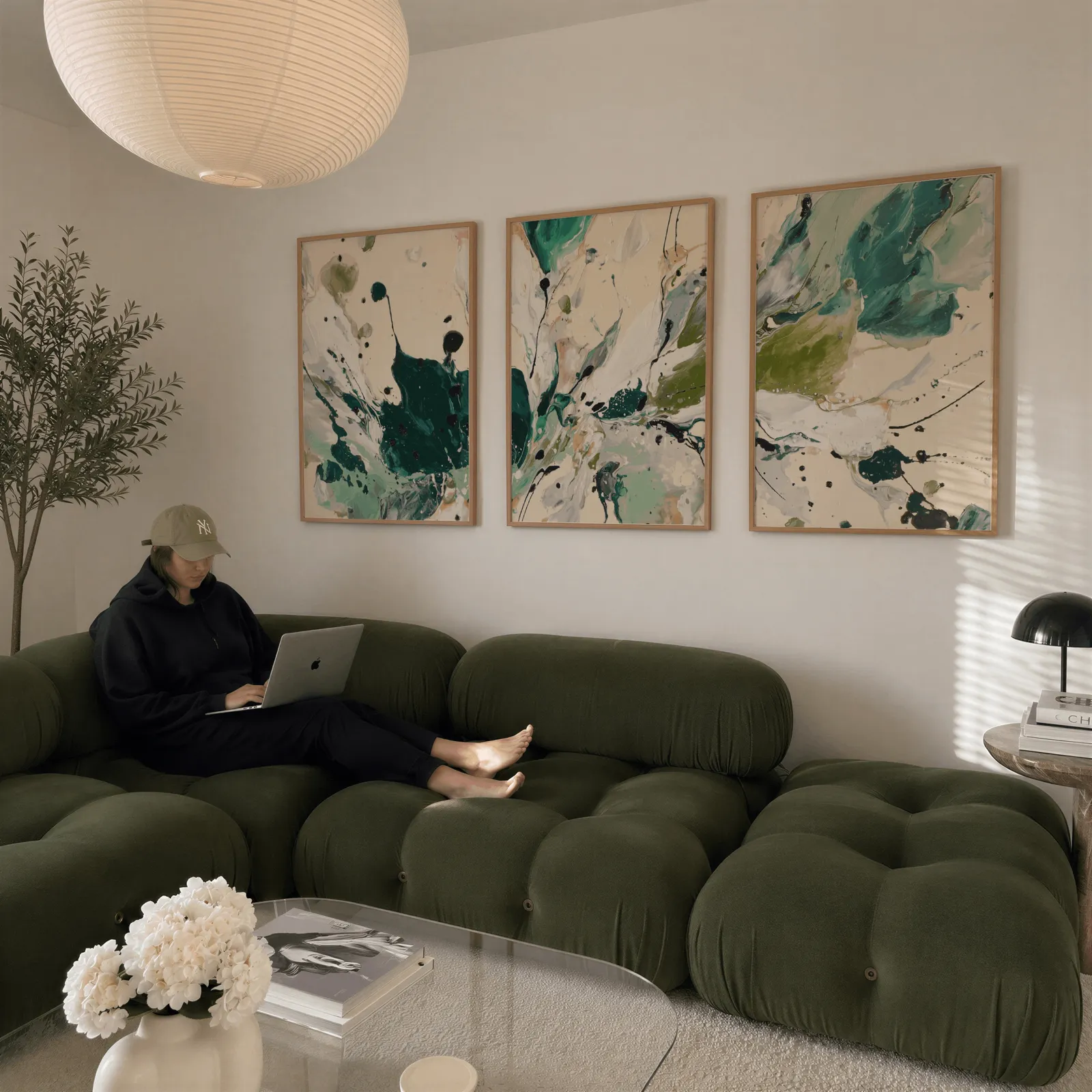 green abstract triptych wall art, above a plush olive velvet sectional beneath a paper lantern light