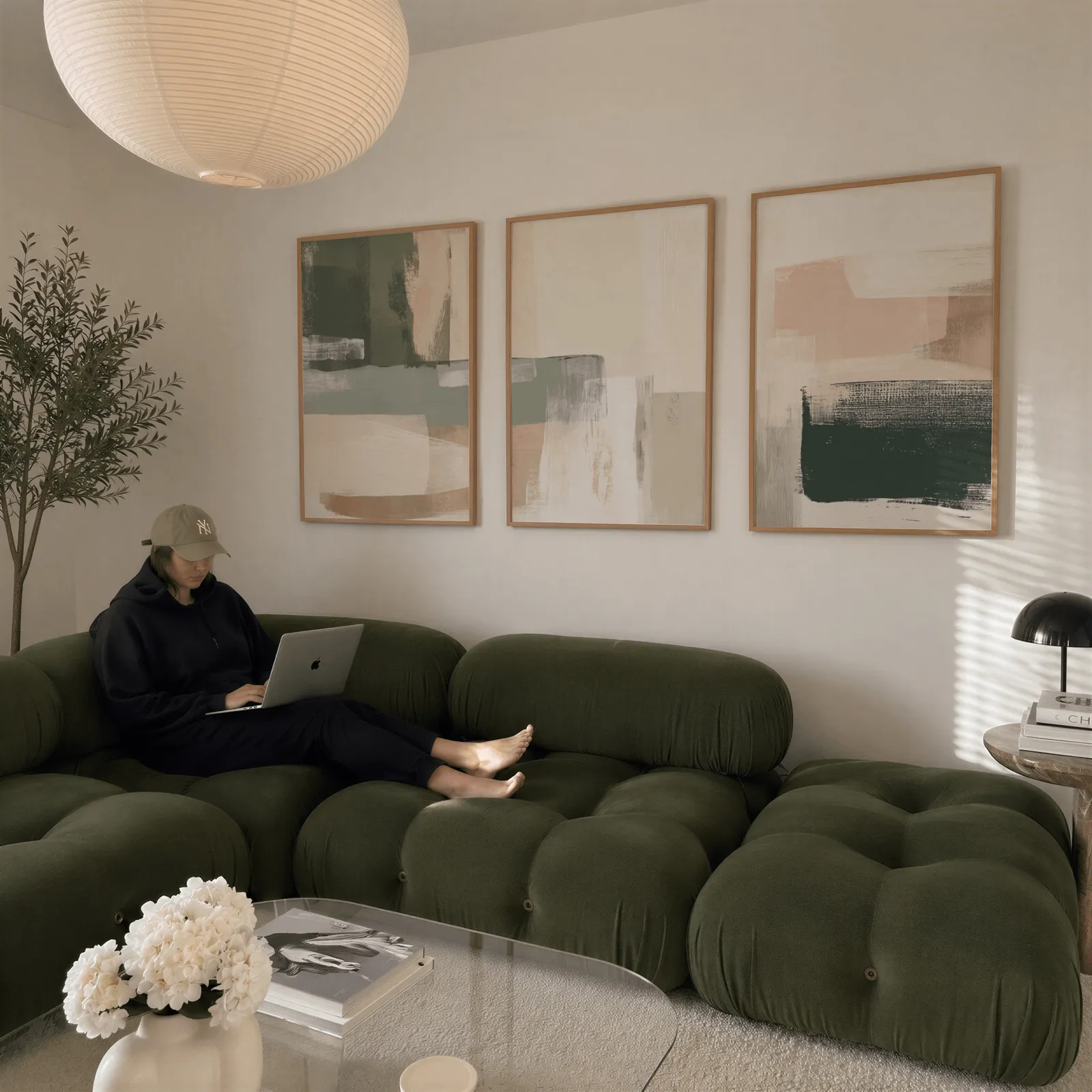 neutral abstract triptych wall art in green and terracotta, above a plush olive velvet sectional beneath a paper lantern light
