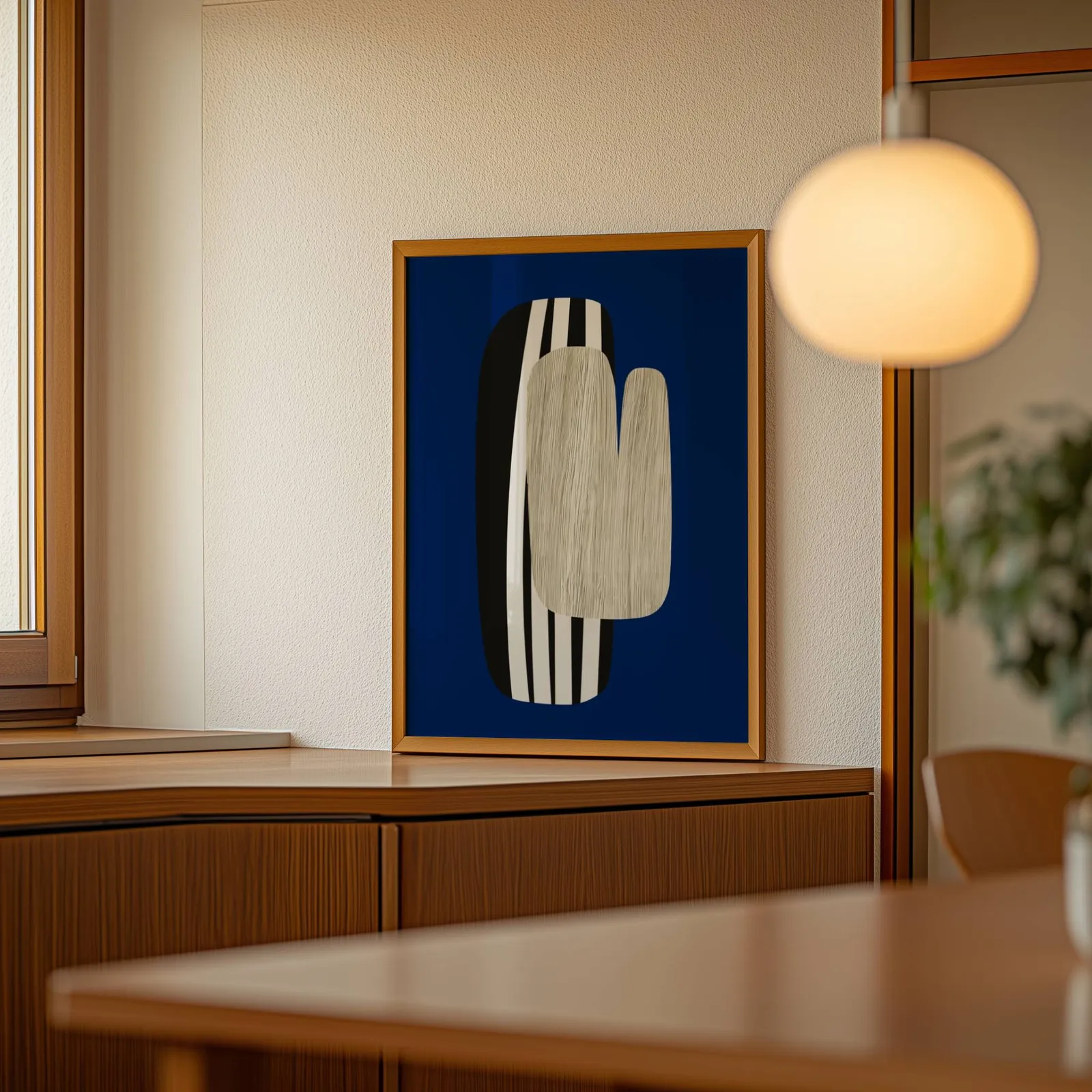 navy blue abstract wall art, leaning on a wooden sideboard beside a glowing globe pendant