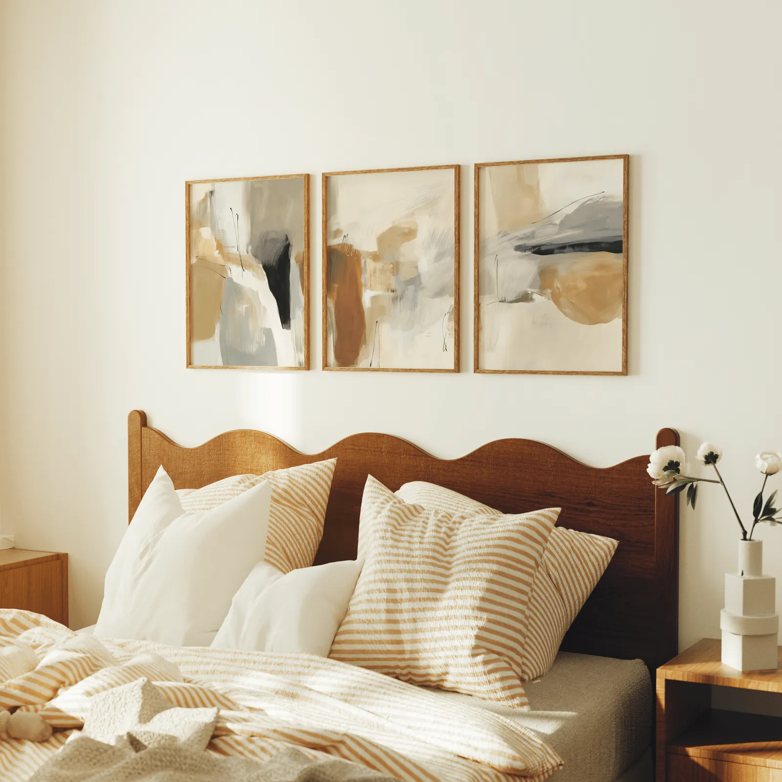 neutral abstract triptych wall art in terracotta and beige, above a scalloped wooden headboard with striped pillows